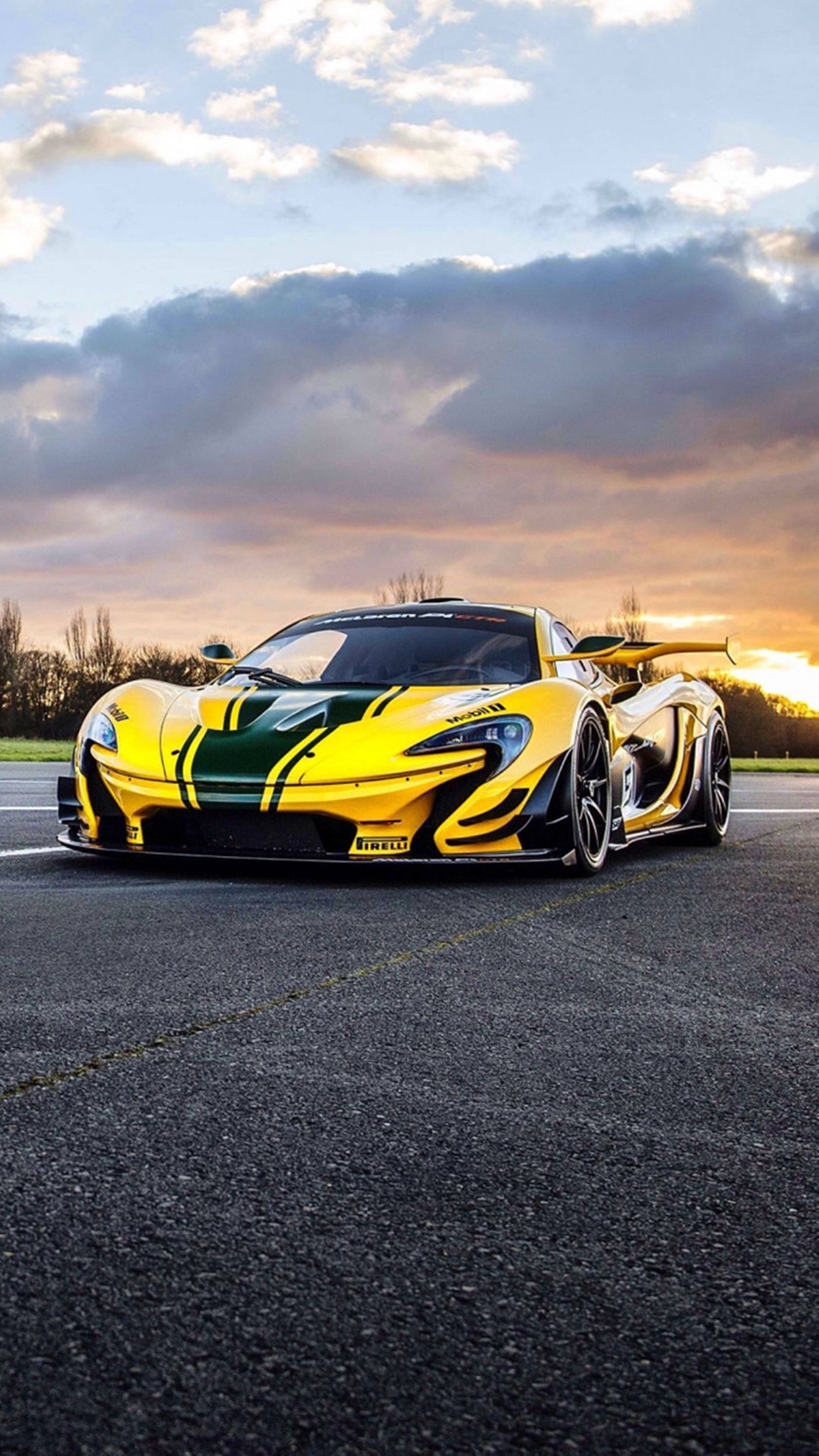 Black And Yellow 桌布 壁紙 — 一輛黃綠色的McLaren P1超級跑車停在瀝青賽道上，背景是壯麗的日落天空，散佈著雲朵。