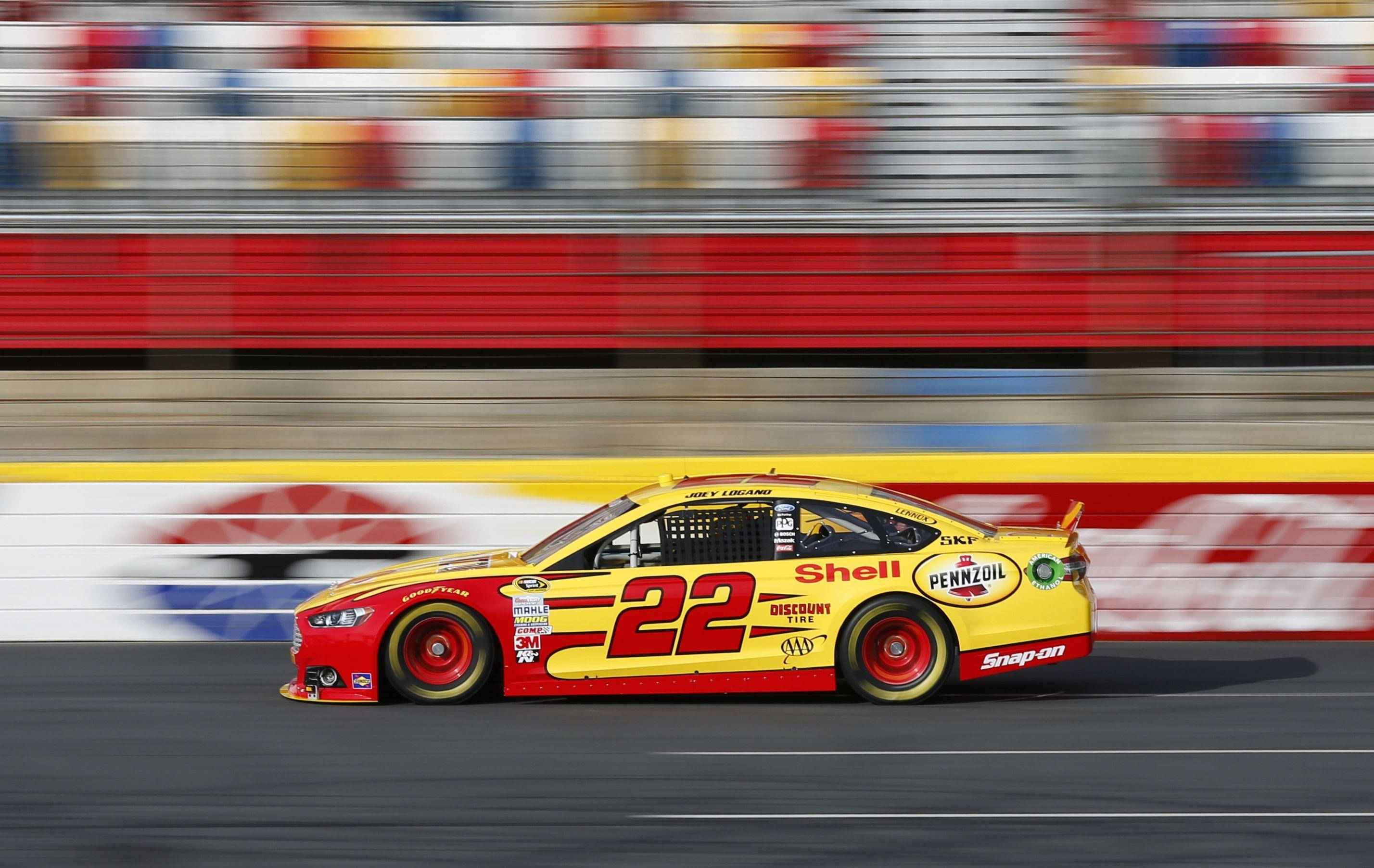 Joey Logano 桌布 壁紙 — 一輛黃色和紅色的NASCAR賽車（22號）在賽道上飛馳，經過模糊的看台。