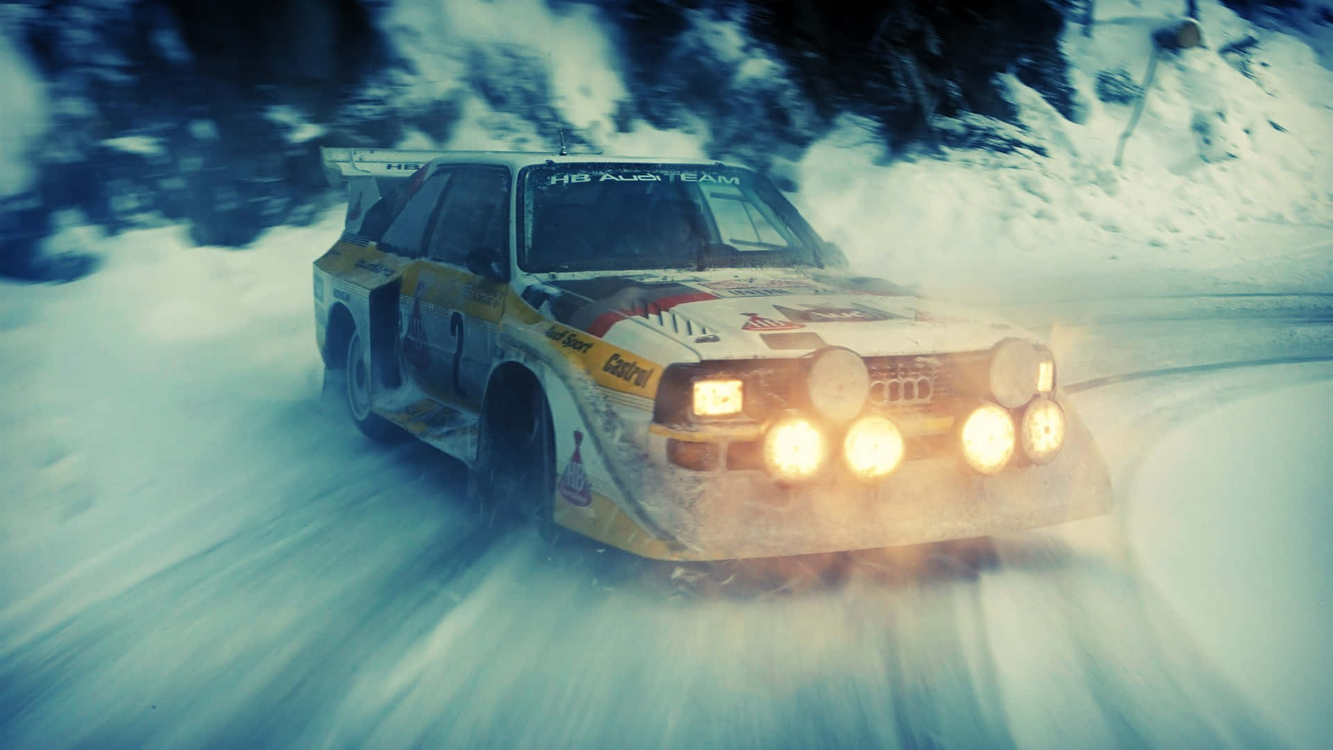 1920x1080 Dirt Rally 桌布 壁紙 — 一輛黃色拉力賽車亮著明亮的頭燈，在白雪覆蓋的森林蜿蜒道路上疾馳，揚起雪霧。