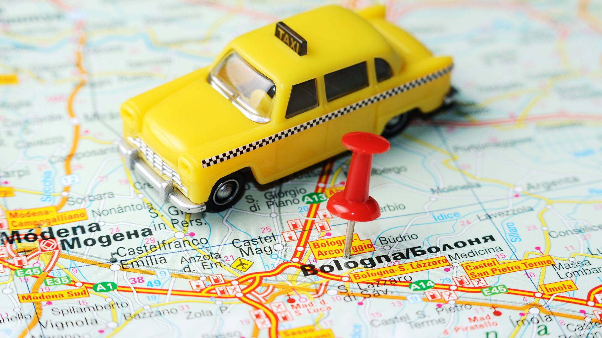 Map 桌布 壁紙 — 一輛黃色玩具計程車放在詳細的義大利地圖上，地圖上有一個紅色大頭針標記波隆那。