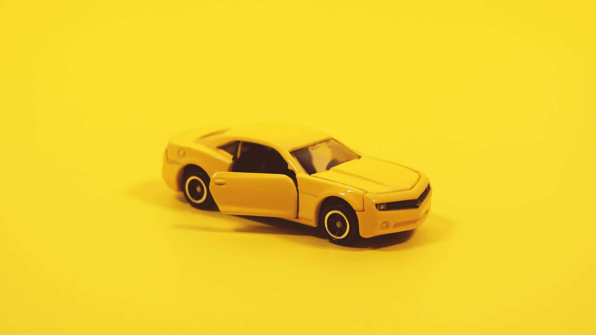 Yellow Car 桌布 壁紙 — 一輛黃色玩具跑車打開車門，居中放置在純黃色背景上。