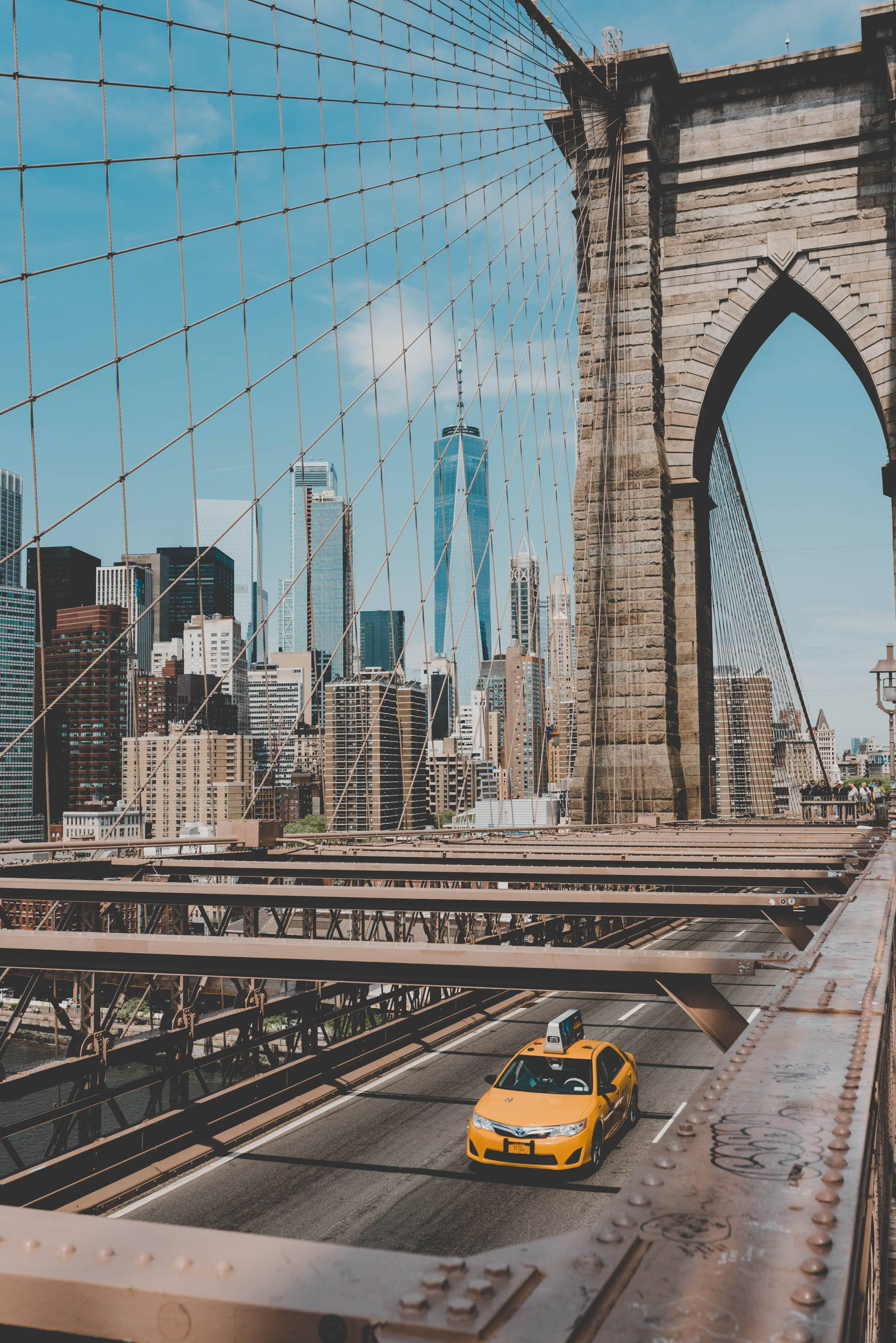 New York 桌布 壁紙 — 一輛黃色的士駛過布魯克林大橋，曼哈頓天際線和世界貿易中心一號樓在晴朗的藍天下清晰可見。