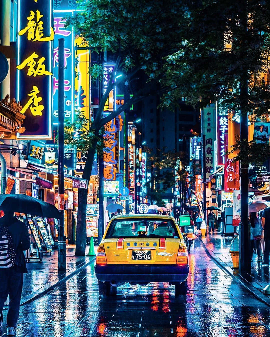 taxi 桌布 壁紙 — 一輛黃色的計程車在夜晚行駛於濕滑的霓虹燈街道上，有發光的招牌和撐傘的行人。