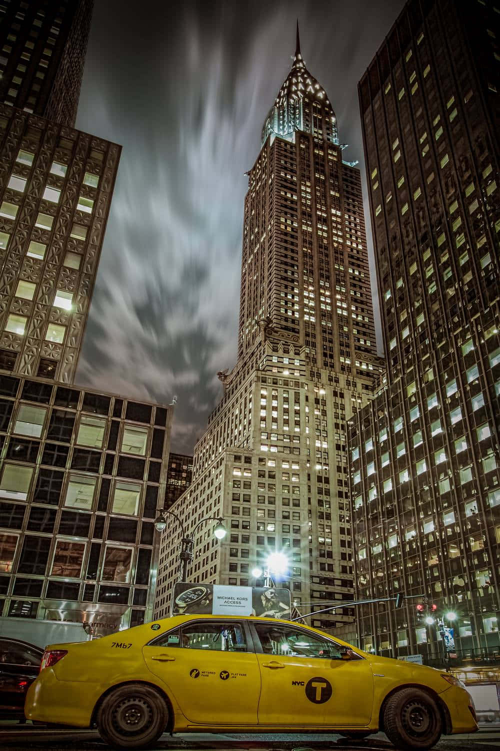 Yellow Cab 桌布 壁紙 — 一輛黃色紐約計程車停泊在夜晚帝國大廈發光的尖頂下，上方有條紋狀的雲。