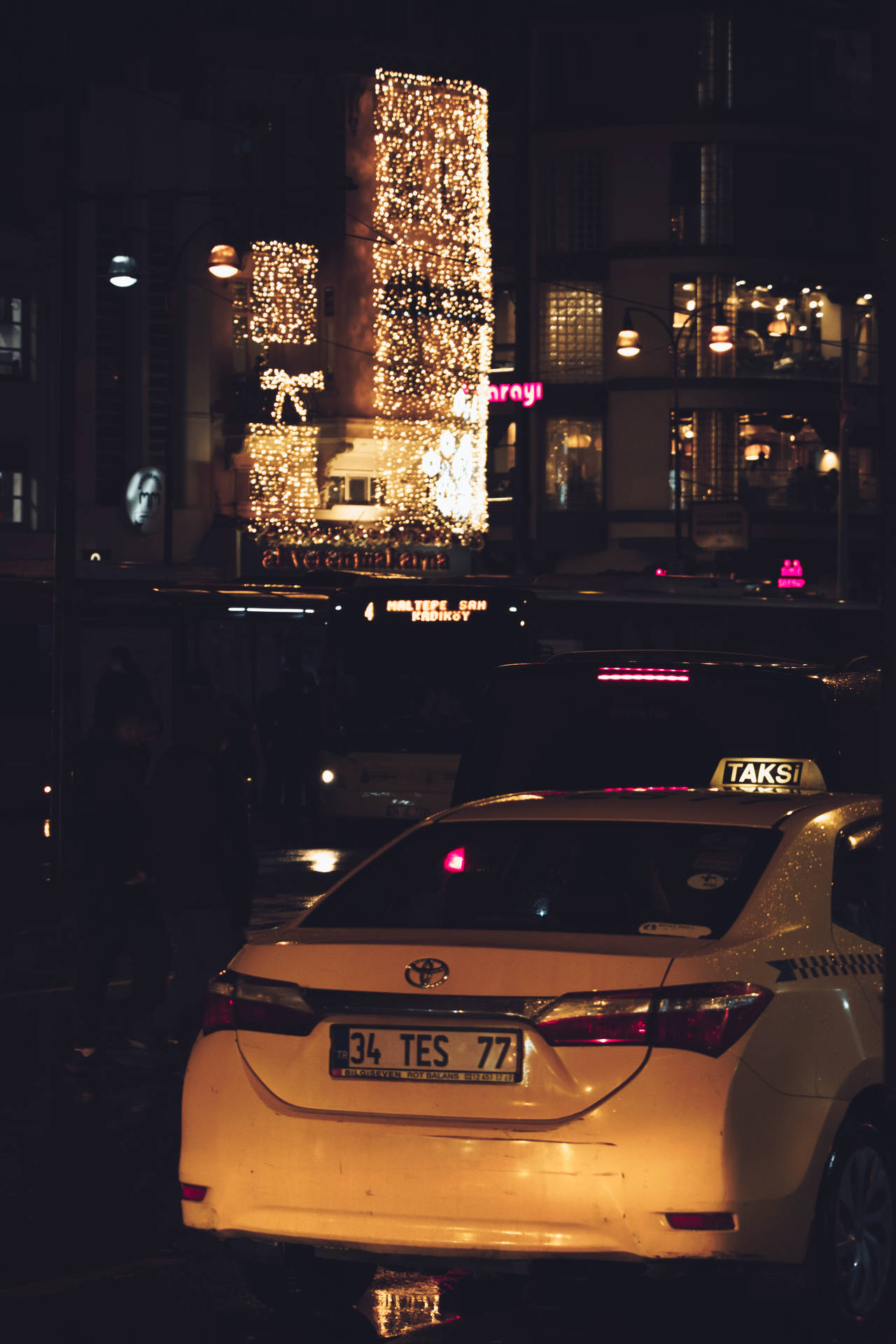 夜晚濕漉漉的城市街道上的黃色計程車，背景是燈火通明的建築。