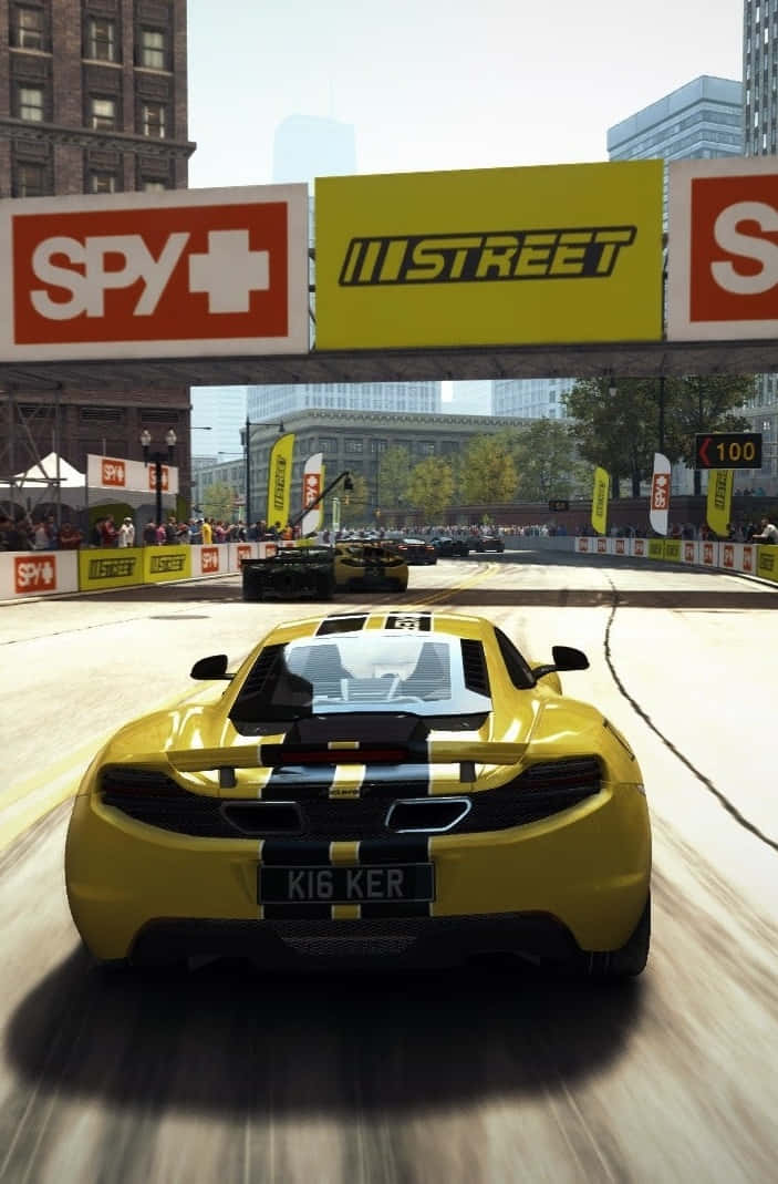 iPhone X Grid Autosport 桌布 壁紙 — 一輛黃色賽車在明亮的日光下，在設有觀眾和品牌橫幅的城市街道賽道上飛馳。