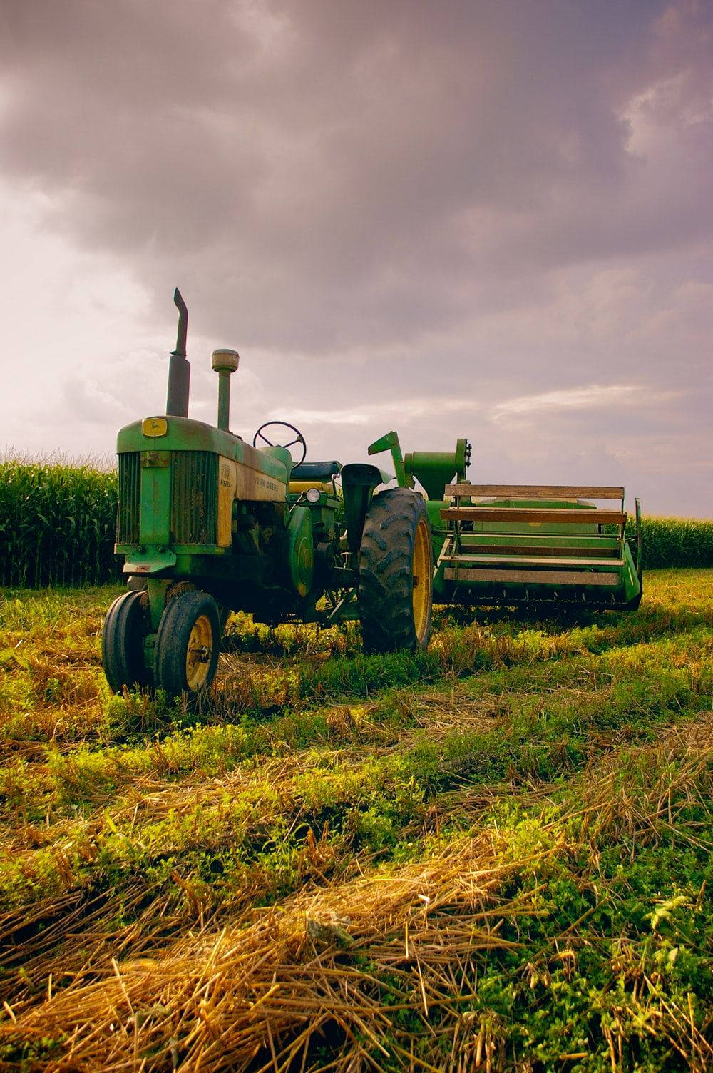 Farmer 桌布 壁紙 — 一輛黃色車輪的復古綠色拖拉機停在收割後的田野上，天空呈現憂鬱的紫色。