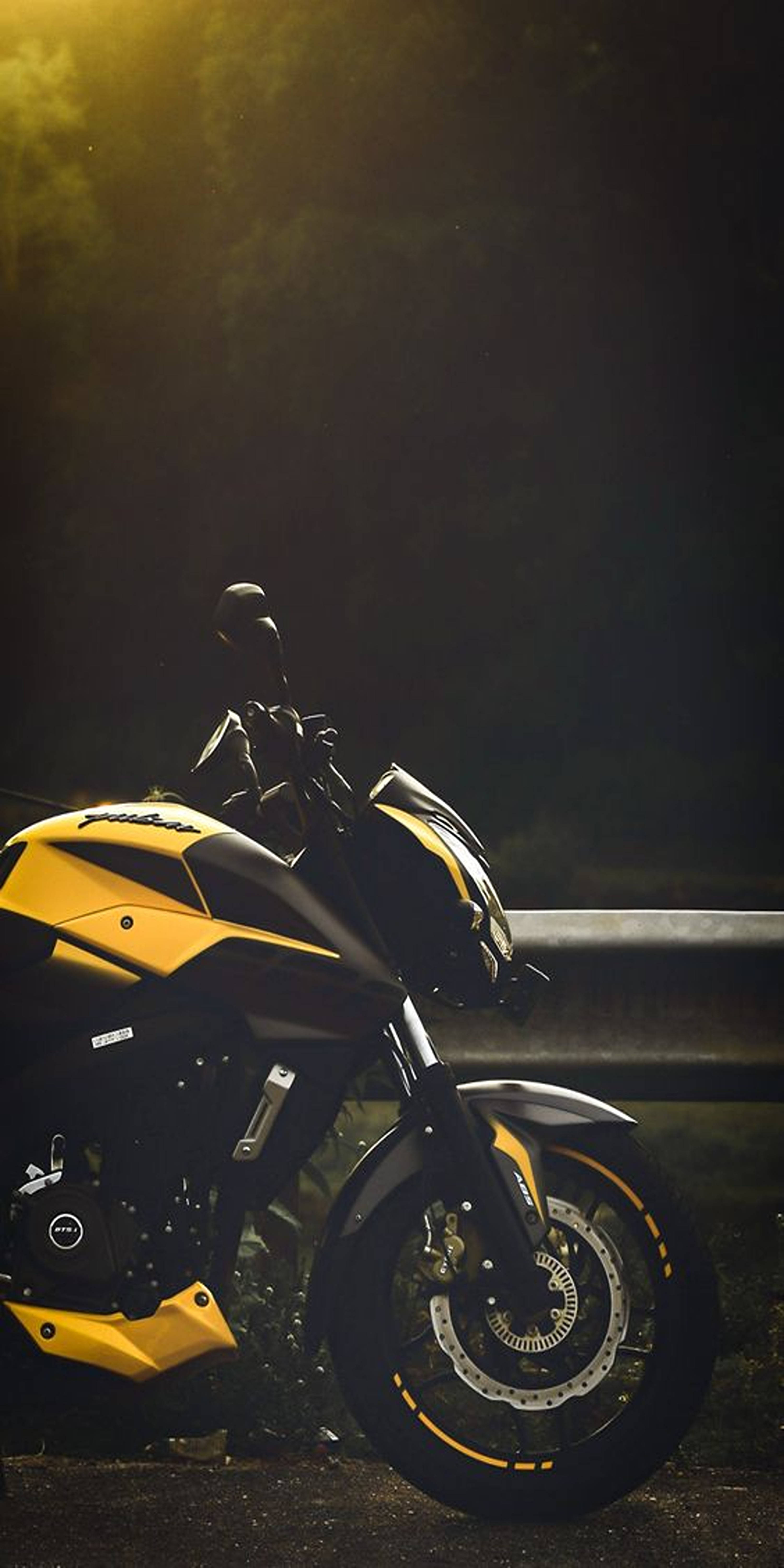 機車 桌布 壁紙 — 一輛黃黑機車在黃昏時分，於黑暗的路邊，沐浴在戲劇性的金色逆光中。