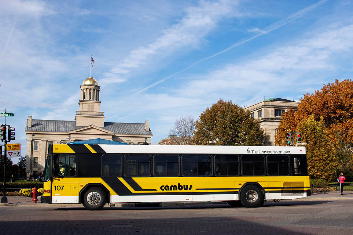 Bus 桌布 壁紙 — 一輛黃黑相間的校園巴士駛過歷史悠久的大學建築，天空湛藍，秋樹環繞。