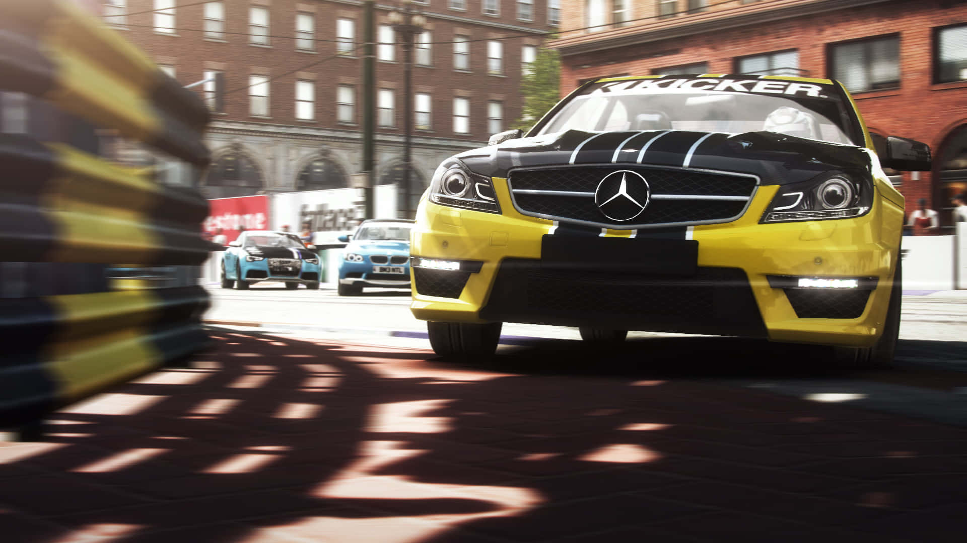 Grid Autosport 桌布 壁紙 — 一輛黃黑相間的梅賽德斯賽車在陽光明媚的磚砌街道上飛馳，經過的護欄和其他賽車手留下動態模糊效果。