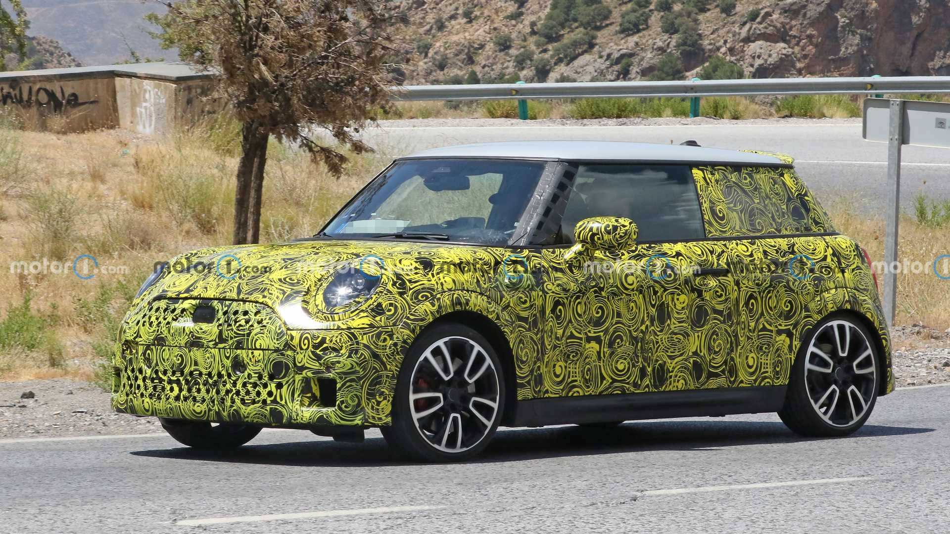 迷幻動圖 桌布 壁紙 — 一輛黃黑迷彩包裹的Mini Cooper原型車在陽光明媚的鄉村道路上行駛，背景有乾草和山丘。