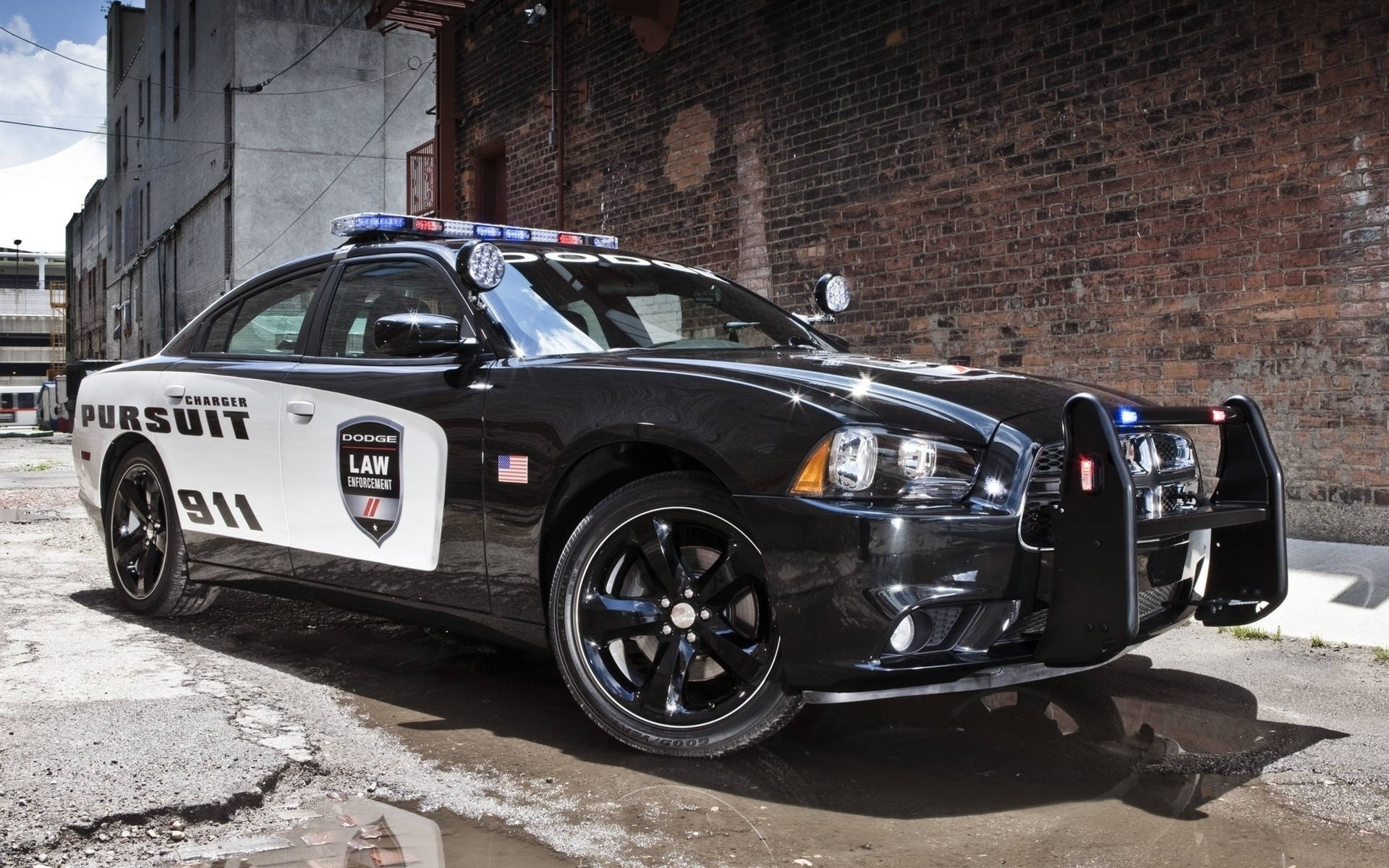 酷炫桌面 桌布 壁紙 — 一輛黑白相間的Dodge Charger Pursuit警車，閃著警燈，停在磚牆旁的濕漉漉的路面上。