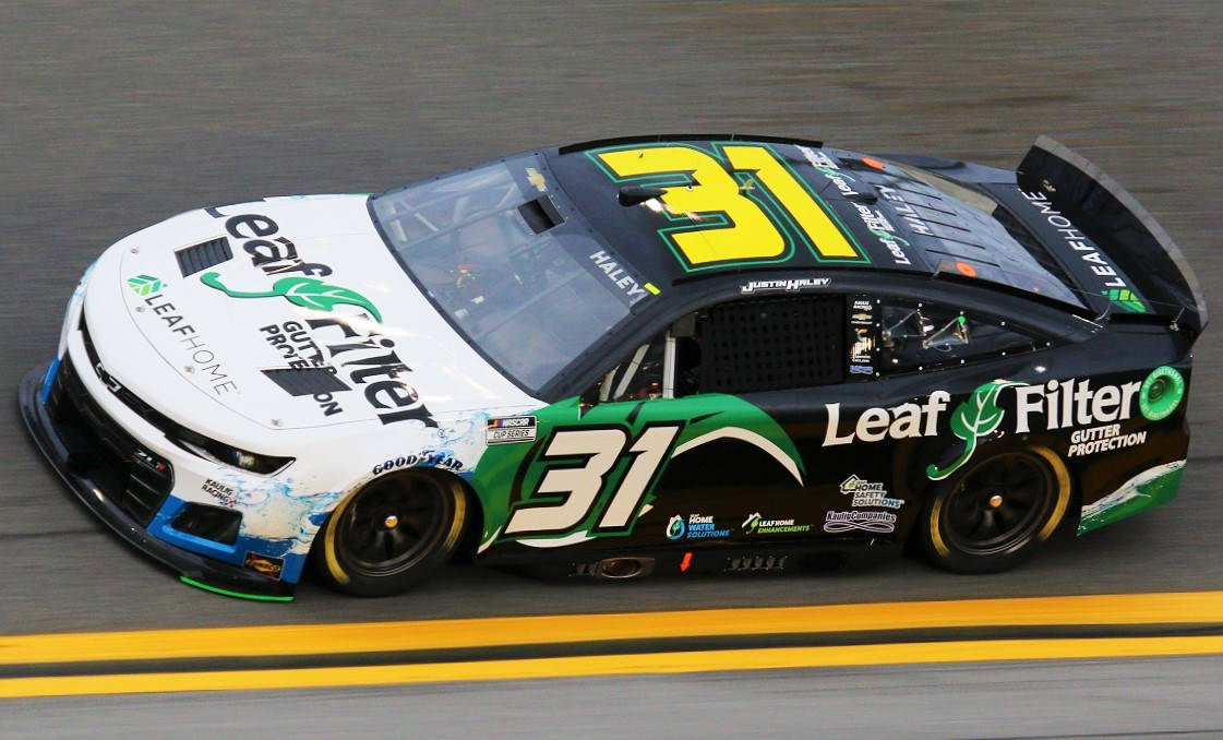 Road 桌布 壁紙 — 一輛黑白相間的NASCAR賽車帶有綠色Leaf Filter品牌標誌，在賽道上高速行駛，呈現動態模糊效果。