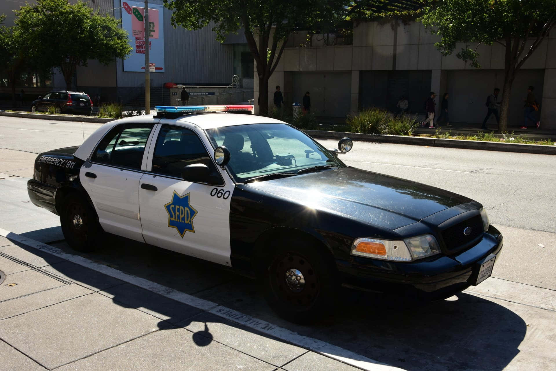 Ford Crown Victoria 桌布 壁紙 — 一輛黑白相間的SEPD警車停放在陽光明媚的城市街道上，背景有樹木和行人。
