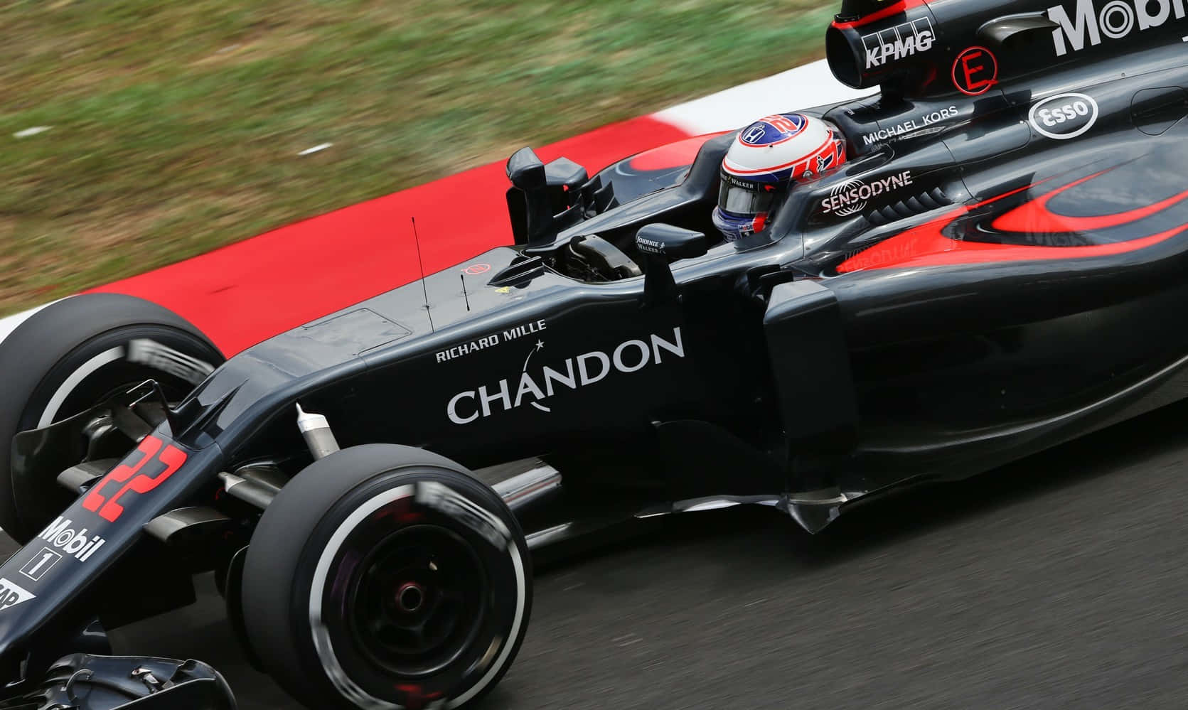HD F1 2016 桌布 壁紙 — 一輛黑紅色的F1賽車在賽道上疾馳，背景是模糊的草地和紅色路緣石。