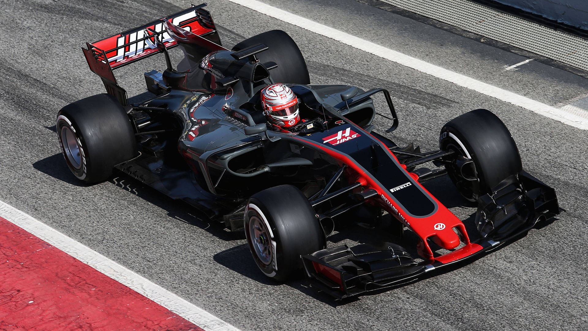 F1 桌布 壁紙 — 一輛黑紅色的Haas F1賽車在明亮的陽光下沿著賽道飛馳，車手戴著頭盔清晰可見。