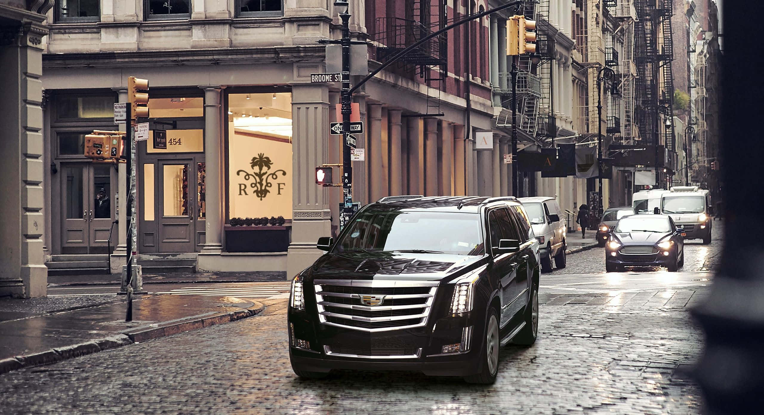 Cadillac Escalade 桌布 壁紙 — 一輛黑色 Cadillac Escalade 在濕滑的鵝卵石街道上行駛，街道兩旁是歷史悠久的磚造建築和商店門面。