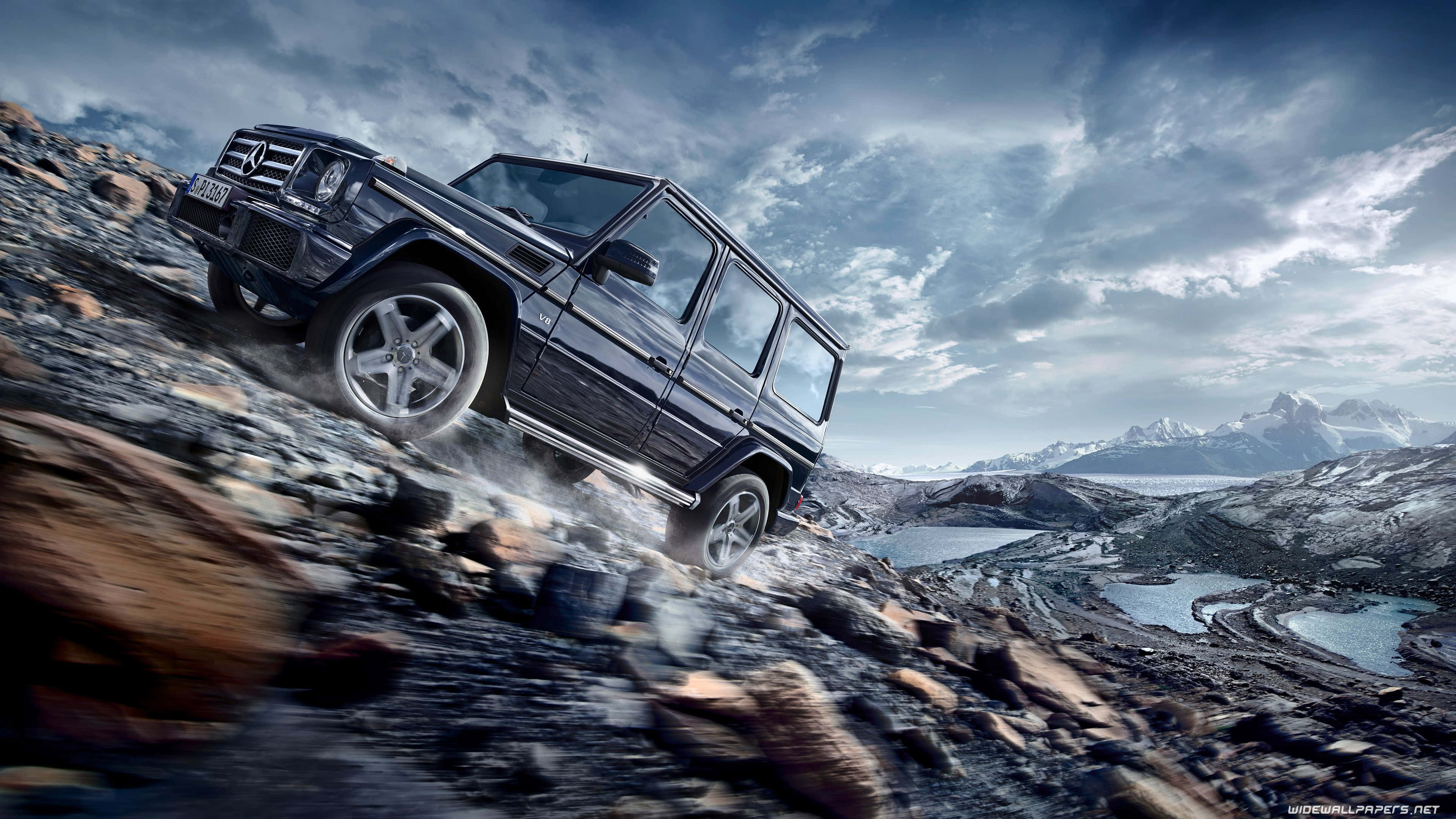 桌布 壁紙 — 一輛黑色 Mercedes G-Class SUV 征服崎嶇的山路，背景是白雪覆蓋的山峰和冰川湖，天空多雲而戲劇化。