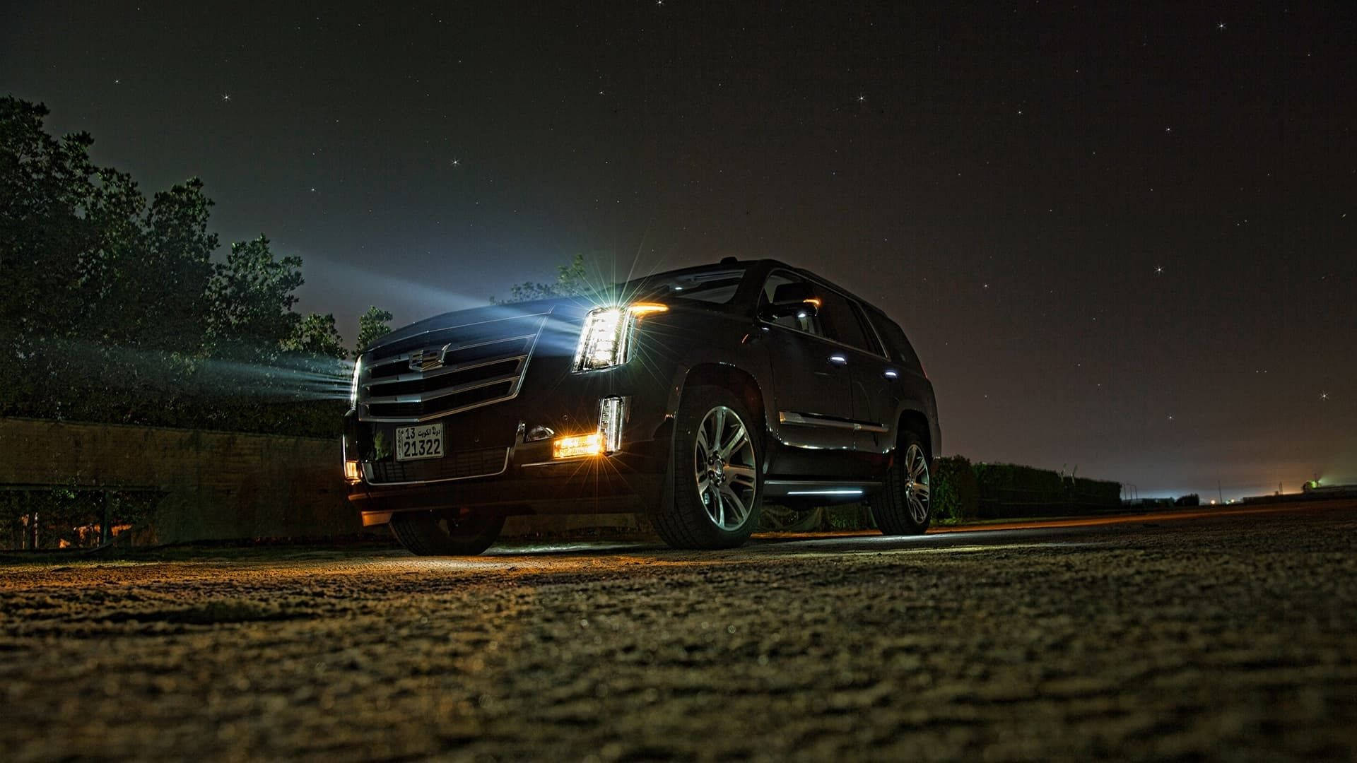 凱迪拉克 桌布 壁紙 — 一輛黑色Cadillac SUV在星空下的碎石路上亮起明亮的車頭燈。