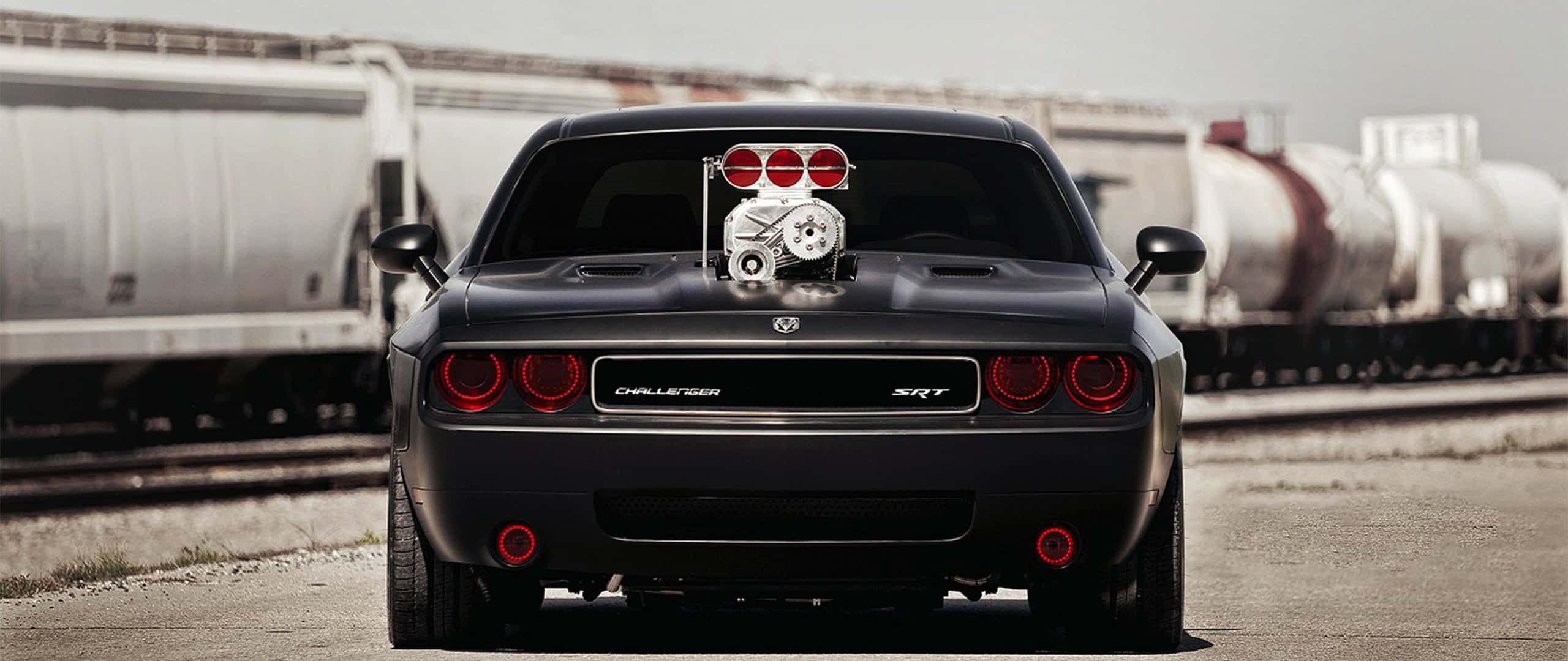 桌布 壁紙 — 一輛黑色Dodge Challenger SRT，引擎蓋上裝有增壓器，停放在火車軌道旁。