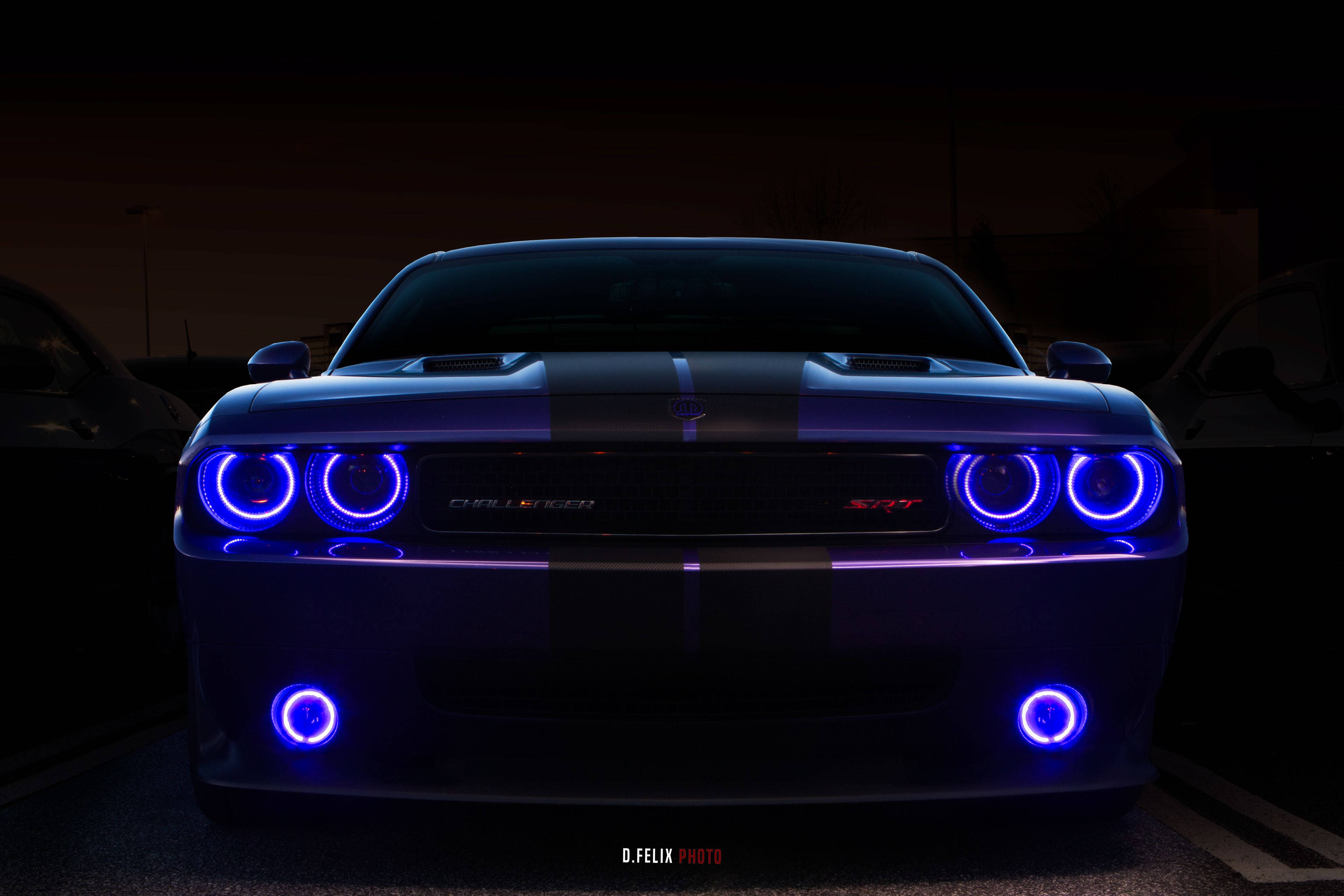 Challenger 桌布 壁紙 — 一輛黑色Dodge Challenger SRT，帶有發光的藍色圓形頭燈和底盤燈，在黑暗的停車場中威嚴地矗立。
