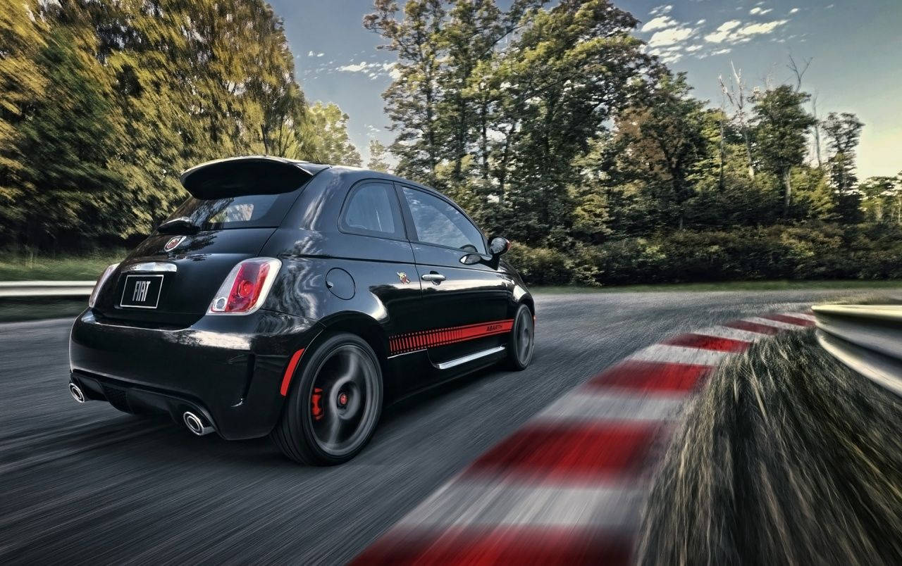 Fiat 桌布 壁紙 — 一輛黑色Fiat 500 Abarth在蜿蜒的森林道路上疾駛，紅白條紋的護欄模糊掠過。