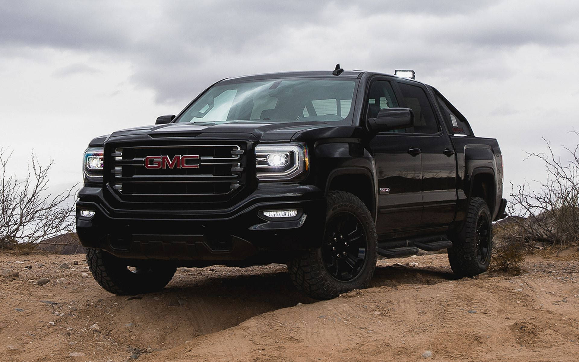Gmc 桌布 壁紙 — 一輛黑色GMC Sierra皮卡車配備越野輪胎，在陰天下一條塵土飛揚的小路上蓄勢待發。