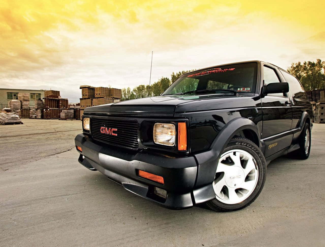 Gmc Syclone 桌布 壁紙 — 一輛黑色GMC Syclone肌肉SUV停在混凝土上，背景是金色夕陽天空和工業煙囪。