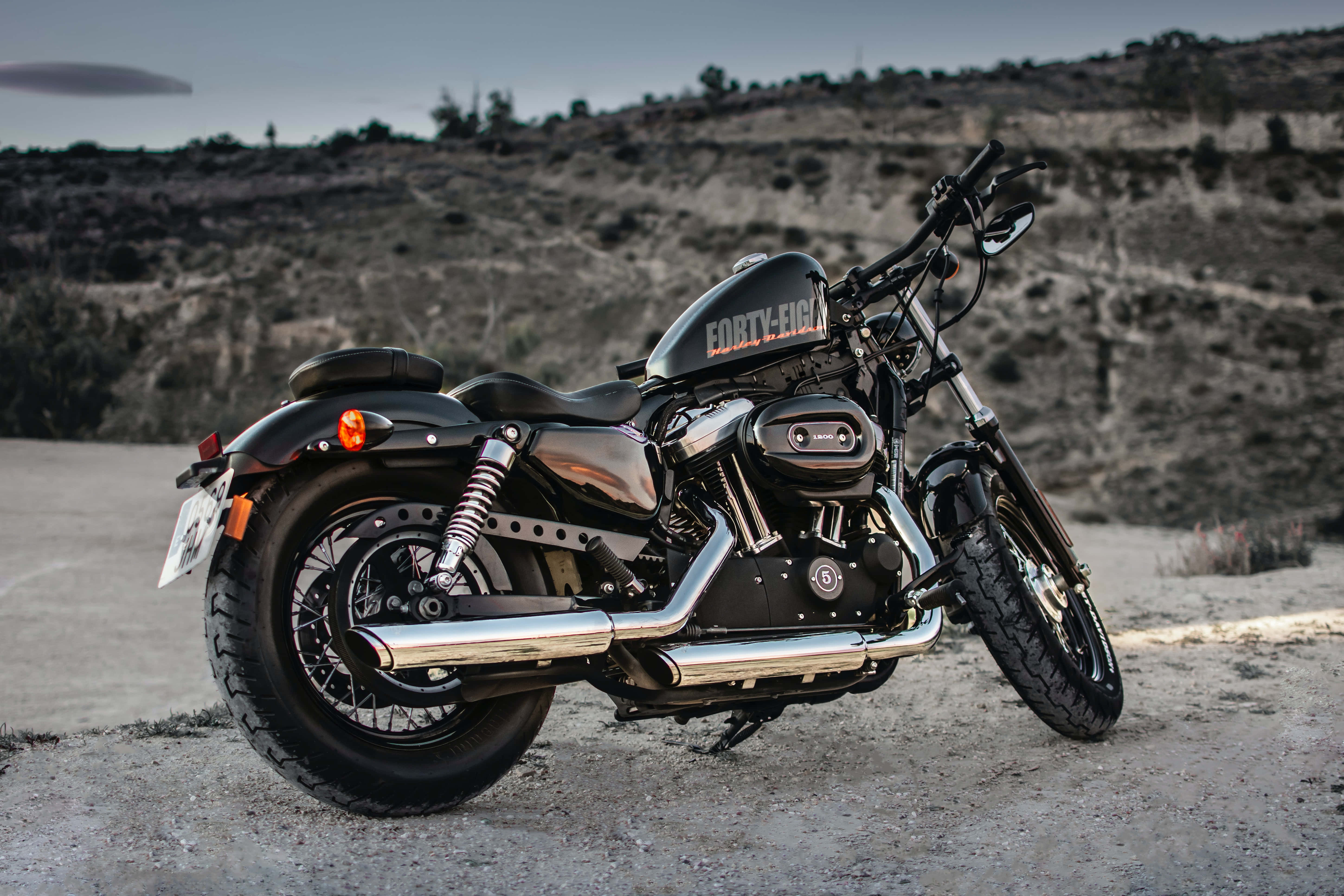 哈雷戴維森 桌布 壁紙 — 一輛黑色Harley-Davidson Forty-Eight摩托車在黃昏時停泊在塵土飛揚的道路上，背景是崎嶇的山丘。