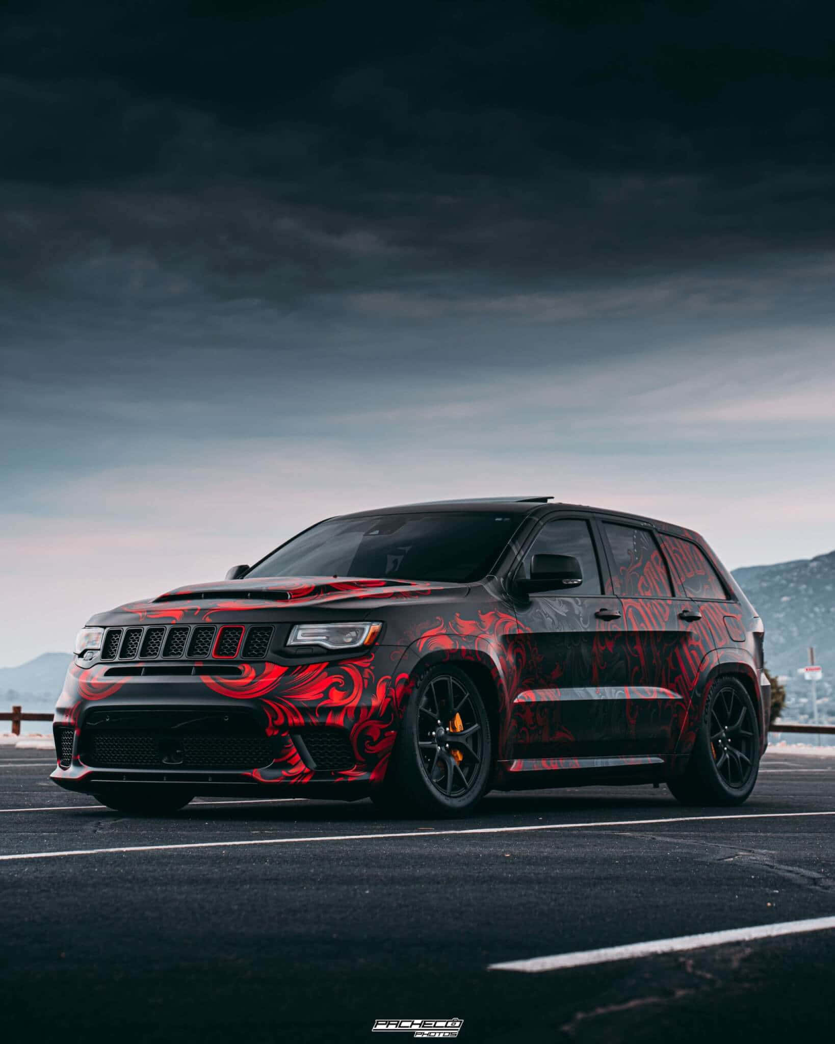 Jeep Trackhawk 桌布 壁紙 — 一輛黑色Jeep Grand Cherokee帶有醒目紅色部落圖案，停泊在空地上，背景是陰鬱的暮色天空。