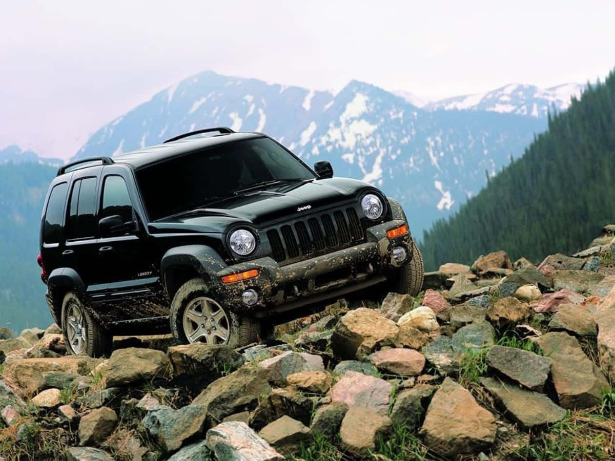 Jeep Liberty 桌布 壁紙 — 一輛黑色Jeep Liberty在崎嶇岩石山路行駛，背景是白雪覆蓋的山峰和茂密森林。