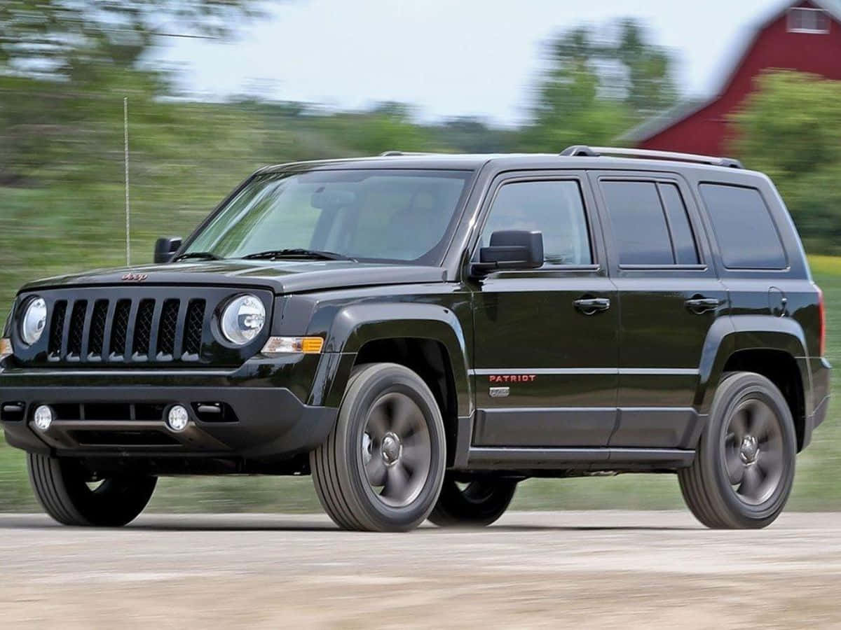 Jeep Patriot 桌布 壁紙 — 一輛黑色Jeep Patriot SUV在綠色樹木和紅色穀倉的背景下高速駛過，帶有動態模糊效果。