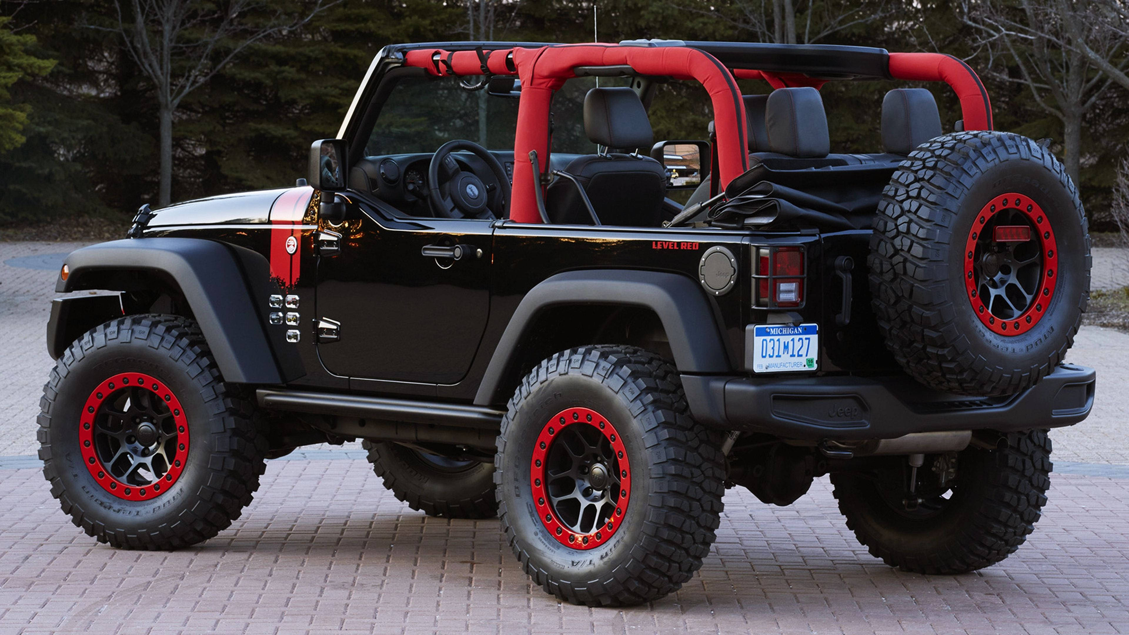 Wrangler 桌布 壁紙 — 一輛黑色Jeep Wrangler，帶有紅色點綴和超大輪胎，停在樹木環繞的磚砌車道上。
