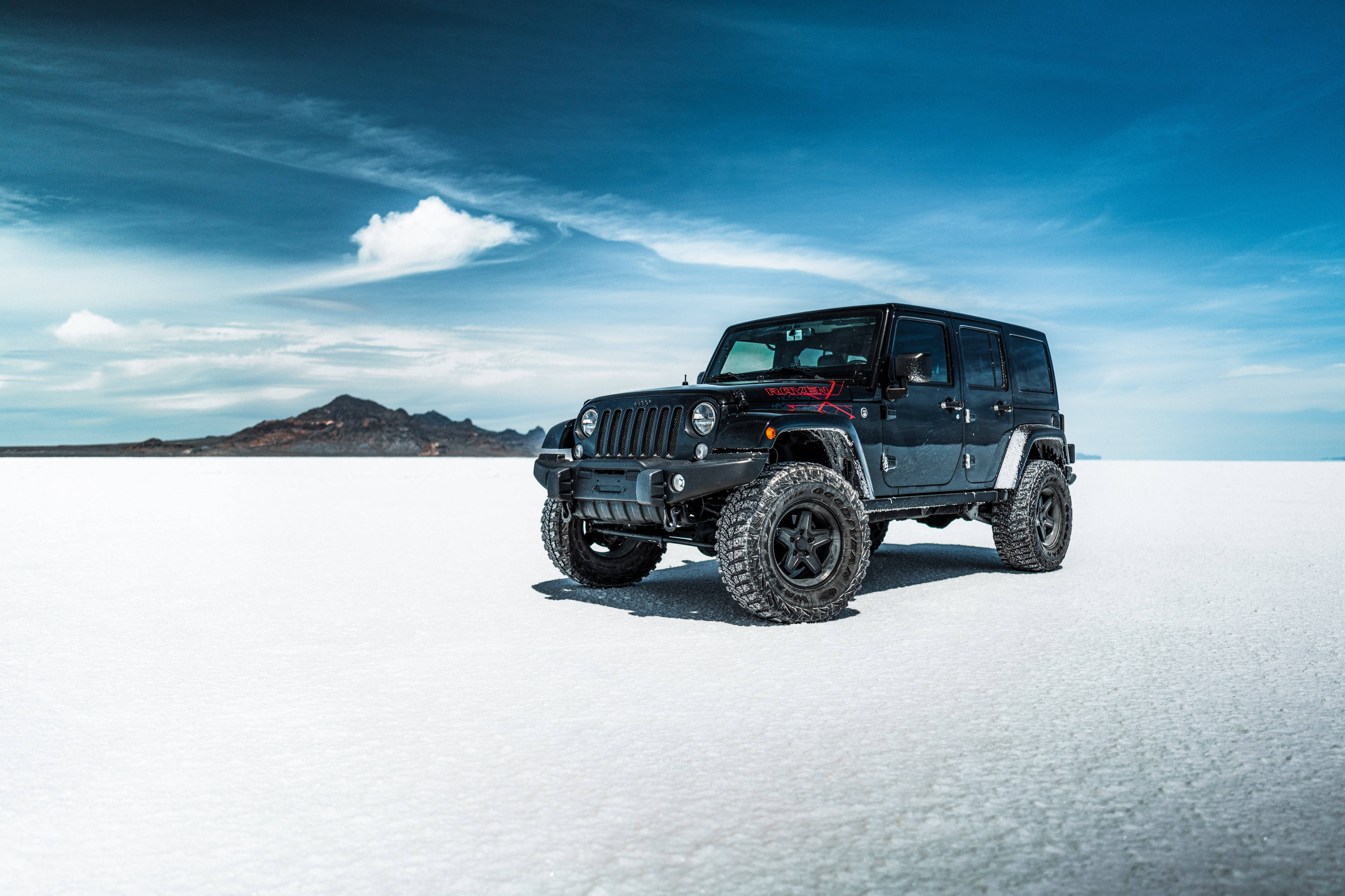 黑色吉普車 桌布 壁紙 — 一輛黑色Jeep Wrangler在廣闊的白色鹽灘上大膽地矗立，背景是戲劇性的藍天和遠山。