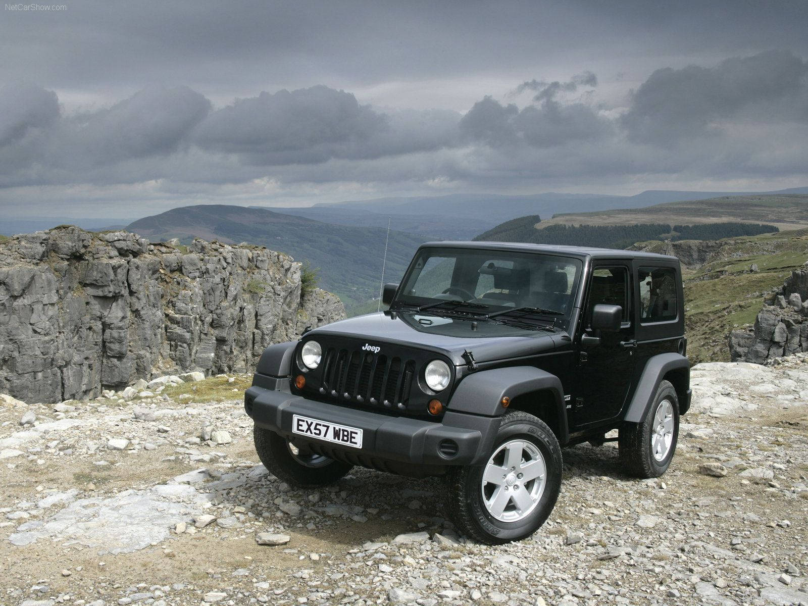 吉普 桌布 壁紙 — 一輛黑色Jeep Wrangler停在岩石懸崖邊緣，俯瞰著陰天下一片廣闊、陰鬱的山地景觀。