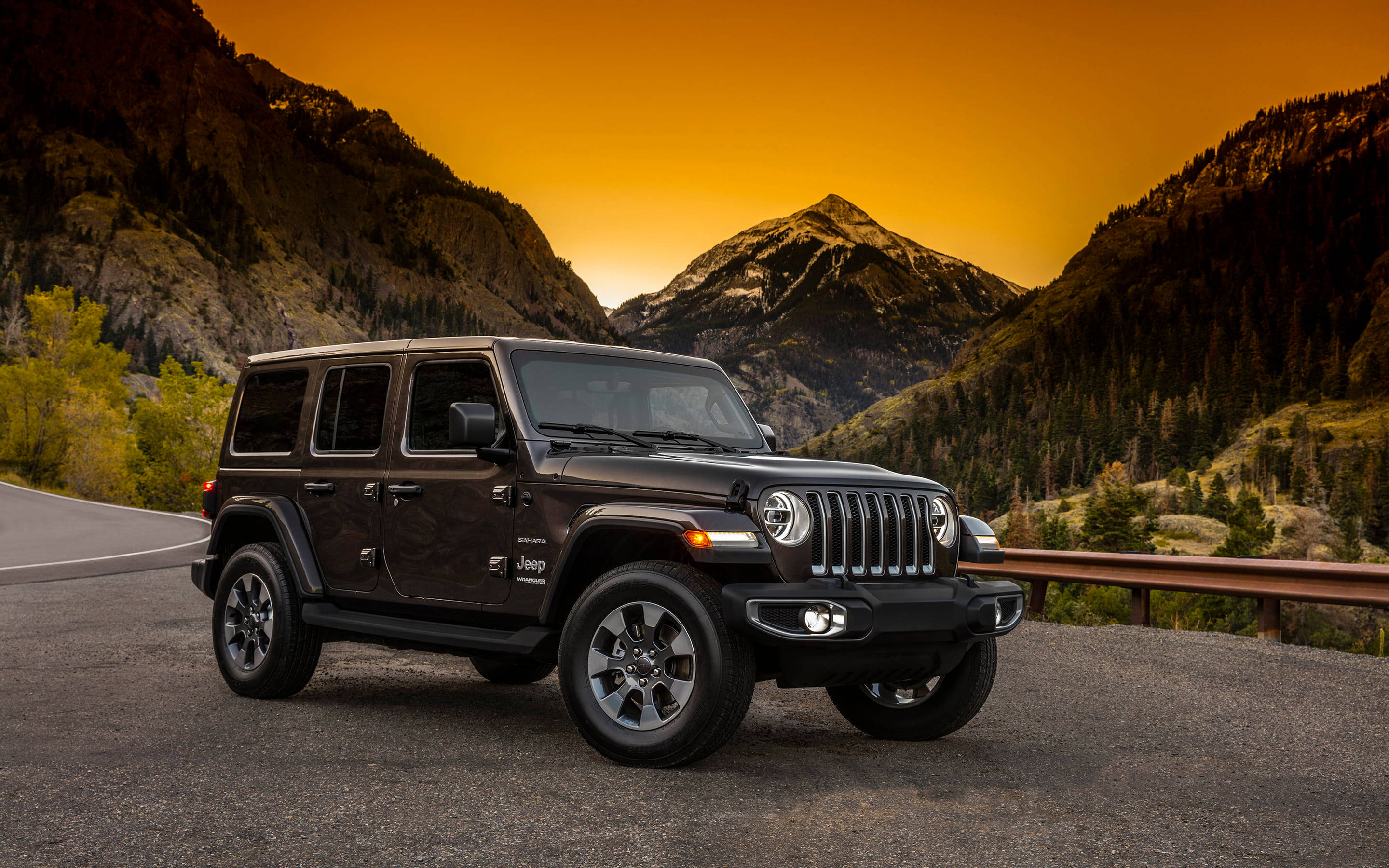 Black Jeep 桌布 壁紙 — 一輛黑色Jeep Wrangler在日落時分停在山路上，背後是橙色的天空和積雪的山峰。