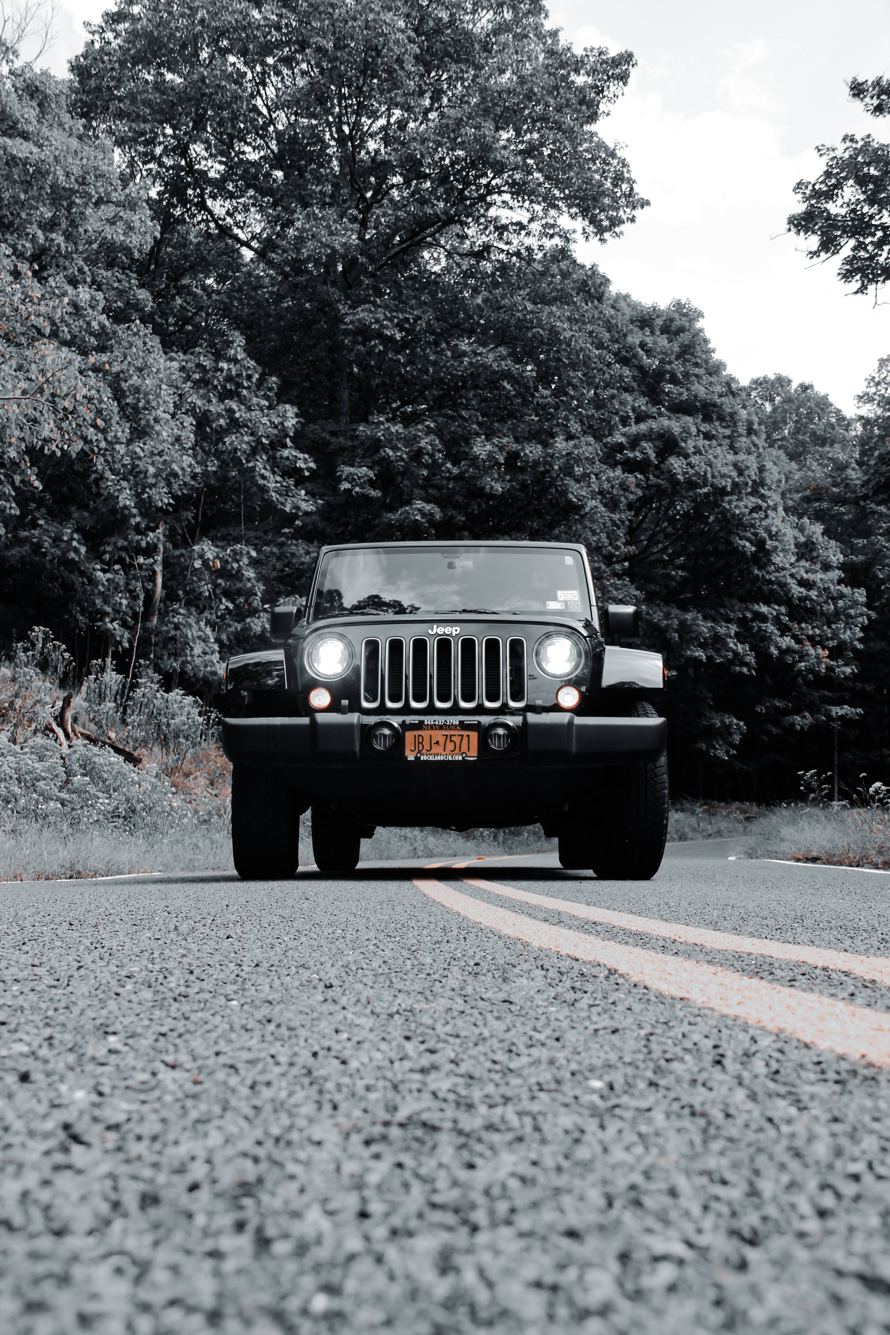 吉普 桌布 壁紙 — 一輛黑色Jeep Wrangler在陰天下行駛在森林道路，車頭燈亮著，朝鏡頭駛來。