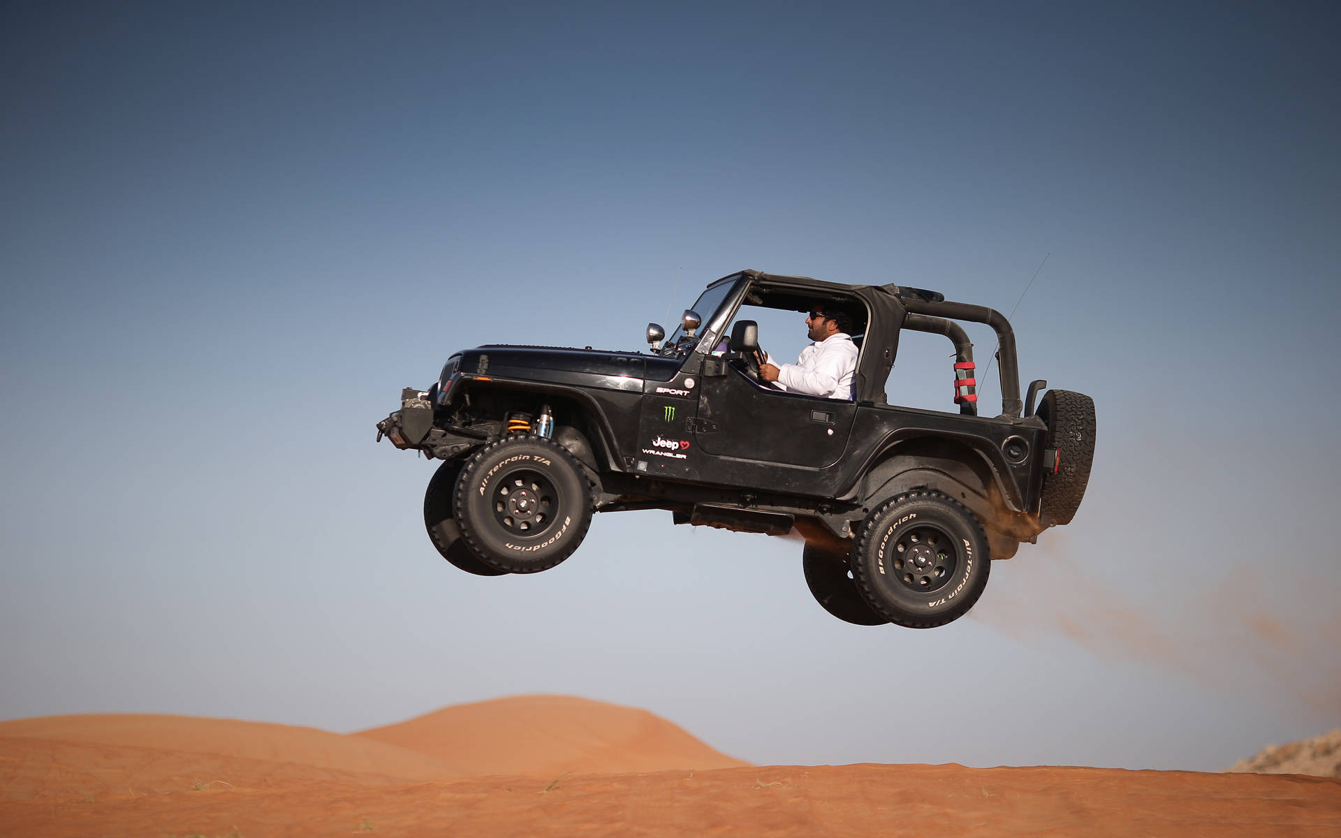 黑色吉普車 桌布 壁紙 — 一輛黑色Jeep Wrangler在金色沙漠沙丘上空飛翔，駕駛正在進行艱險的越野跳躍。