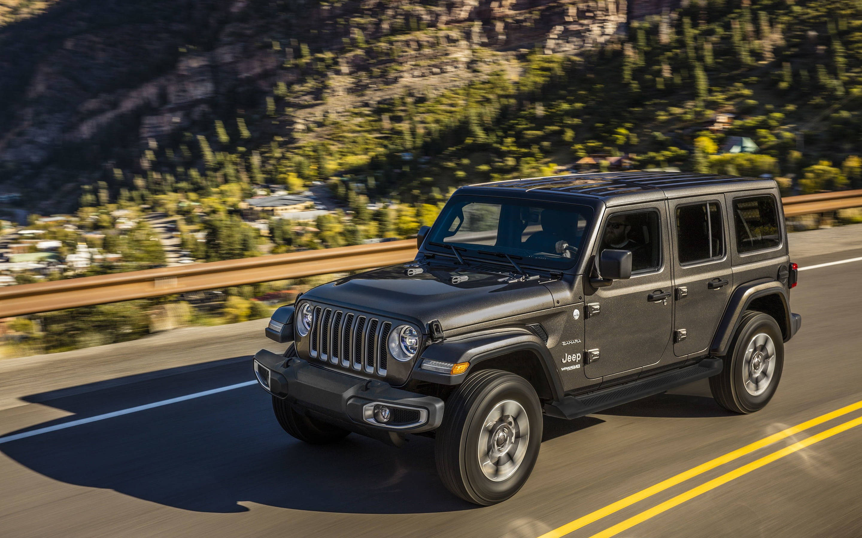 黑色吉普車 桌布 壁紙 — 一輛黑色Jeep Wrangler沿著蜿蜒的山路行駛，背景是茂密的綠色森林和岩石峭壁。