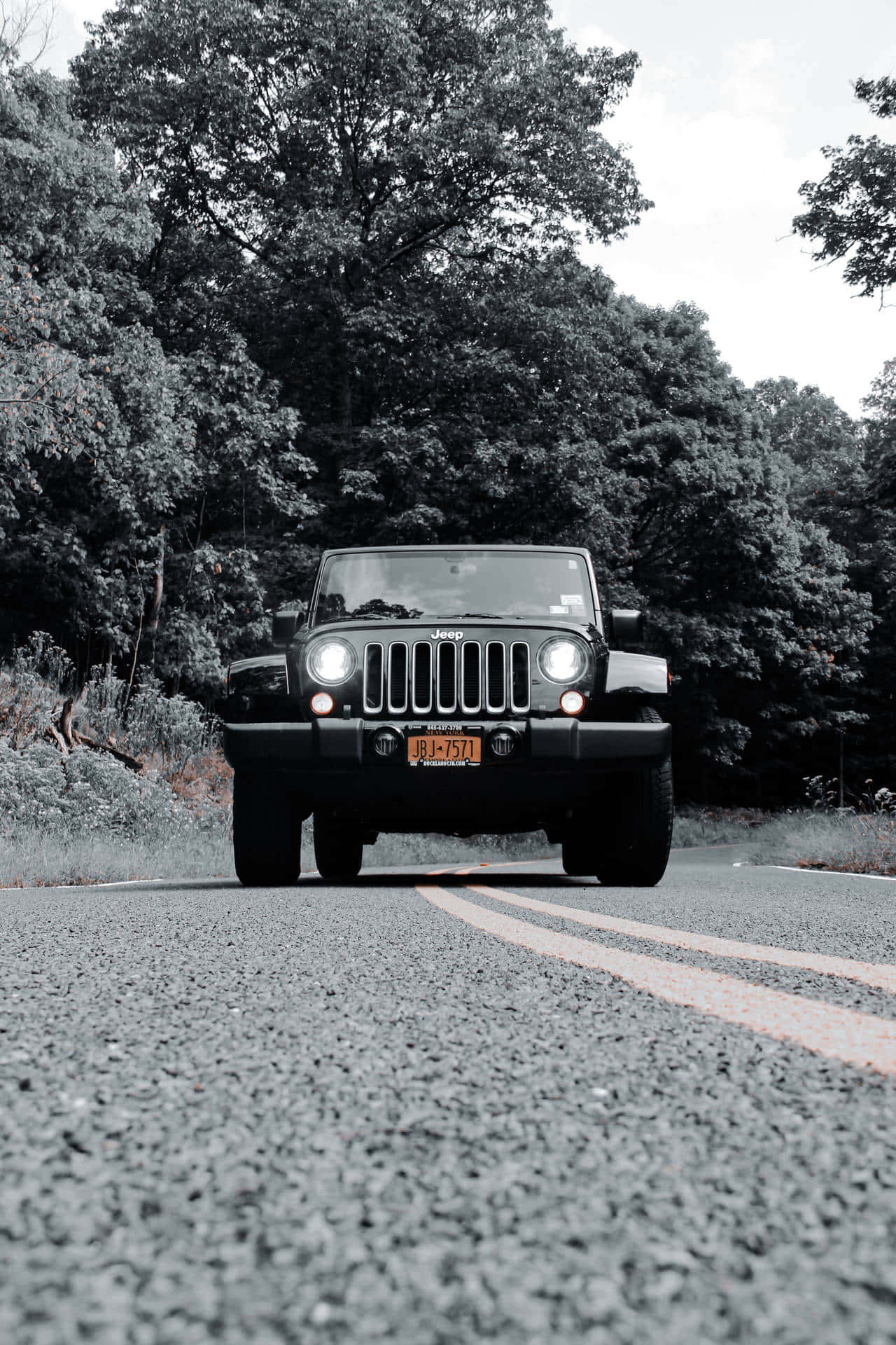吉普 桌布 壁紙 — 一輛黑色Jeep Wrangler在樹木成蔭的道路上迎面駛來，車頭燈閃爍，並帶有單色濾鏡。