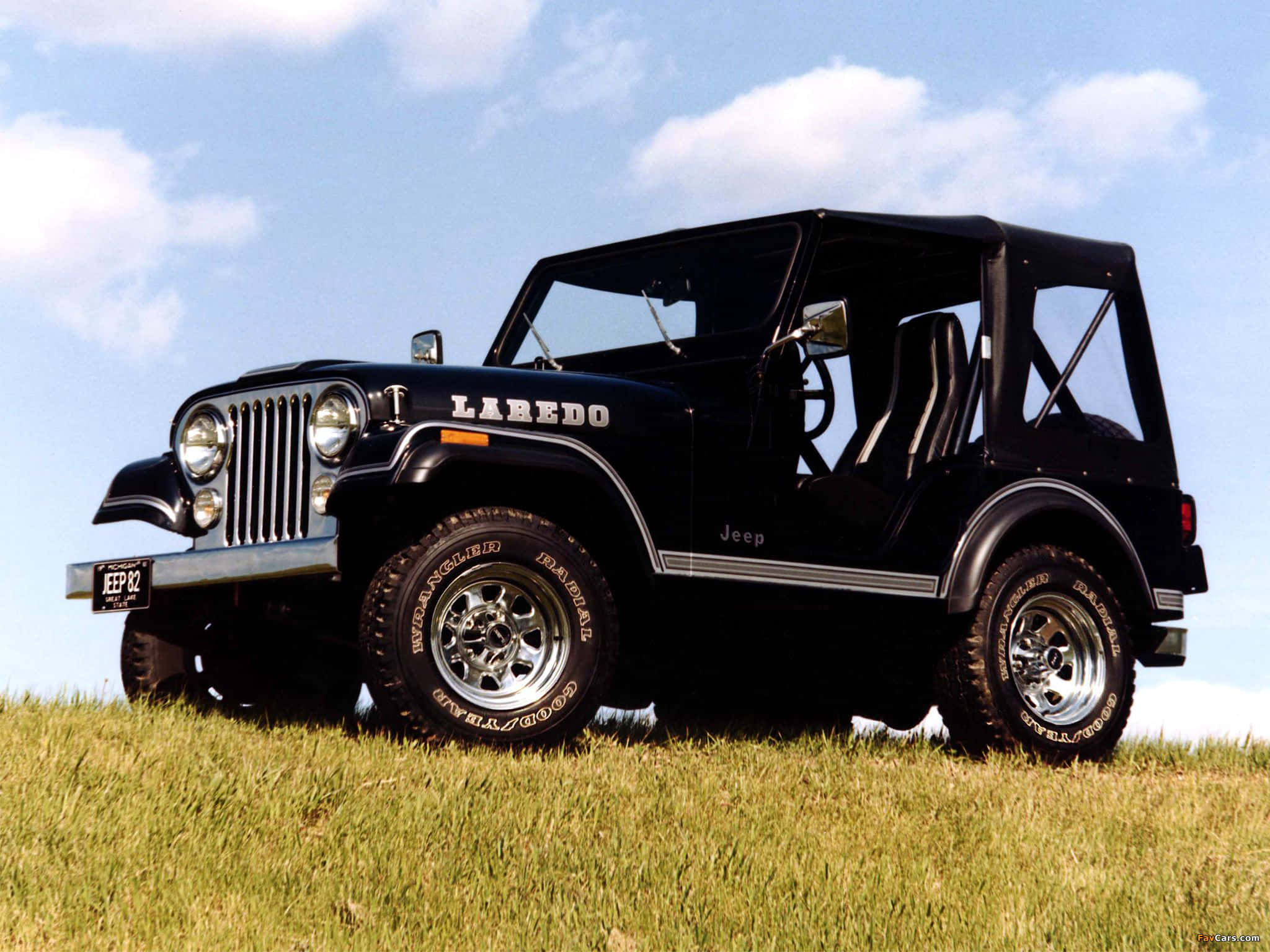 Jeep Cj 桌布 壁紙 — 一輛黑色Jeep Wrangler Laredo自豪地矗立在陽光照耀的草地上，天空湛藍，白雲朵朵。