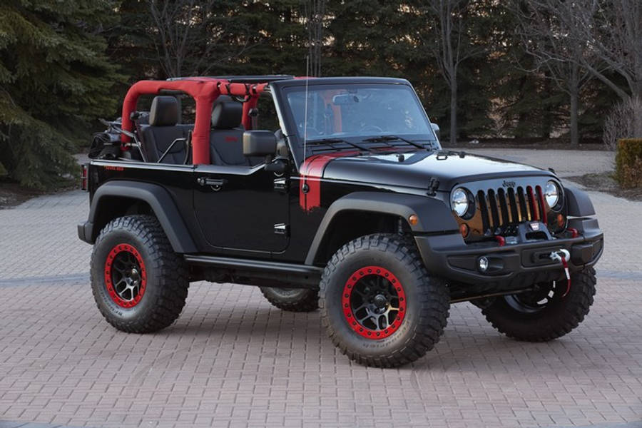 黑色吉普車 桌布 壁紙 — 一輛黑色Jeep Wrangler，帶有紅色點綴和超大輪胎，停在鋪砌的車道上，周圍環繞著樹木。