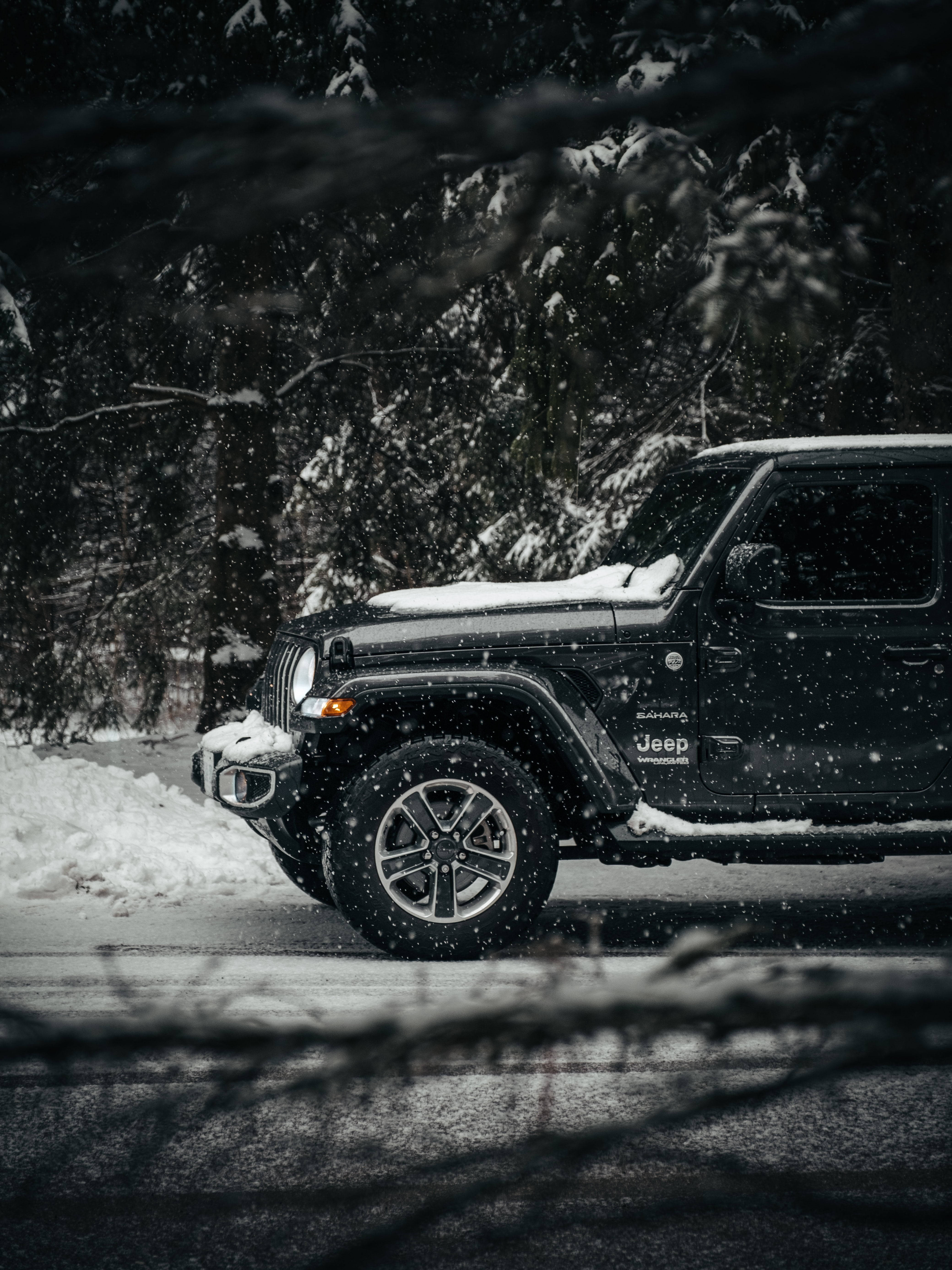 Black Jeep 桌布 壁紙 — 一輛黑色Jeep Wrangler停泊在雪路上，周圍是白雪覆蓋的松樹，正值冬季降雪。