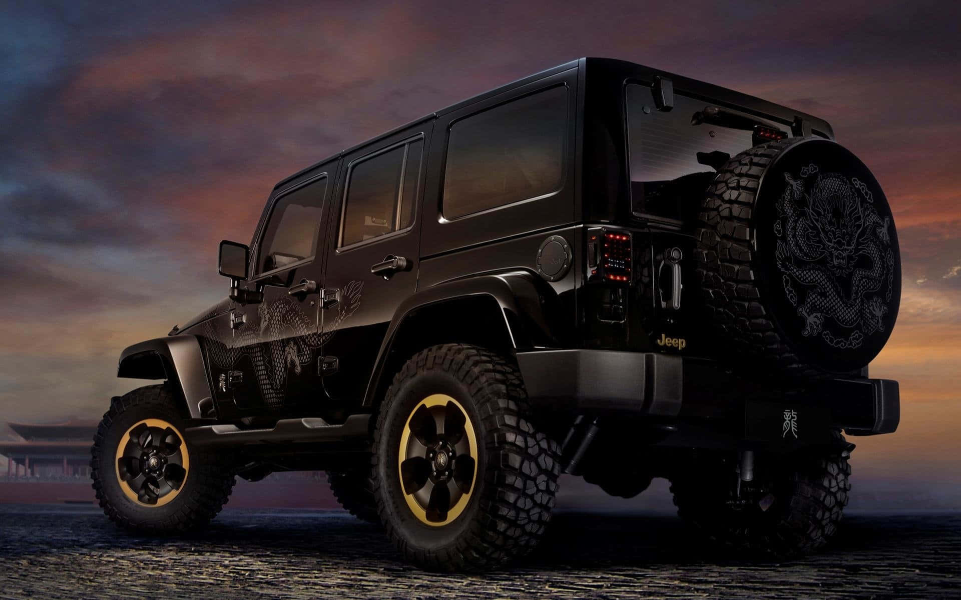 黑色吉普車 桌布 壁紙 — 一輛黑色Jeep Wrangler配金色輪圈和龍形貼紙，停在鵝卵石路上，背景是戲劇性的黃昏天空。