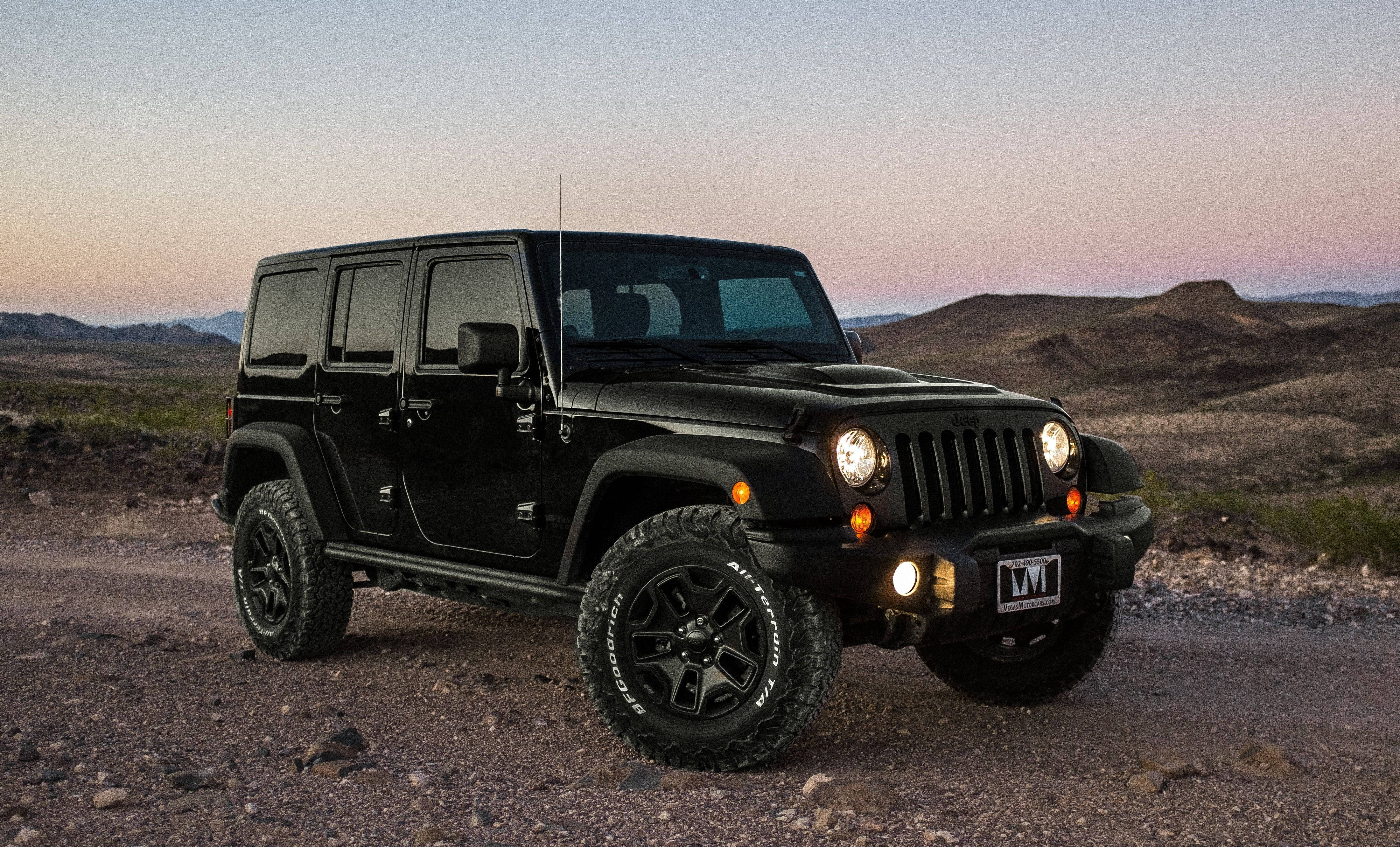 Wrangler 桌布 壁紙 — 一輛黑色Jeep Wrangler在岩石沙漠小徑上，在柔和暮色天空和遠山背景下蓄勢待發。