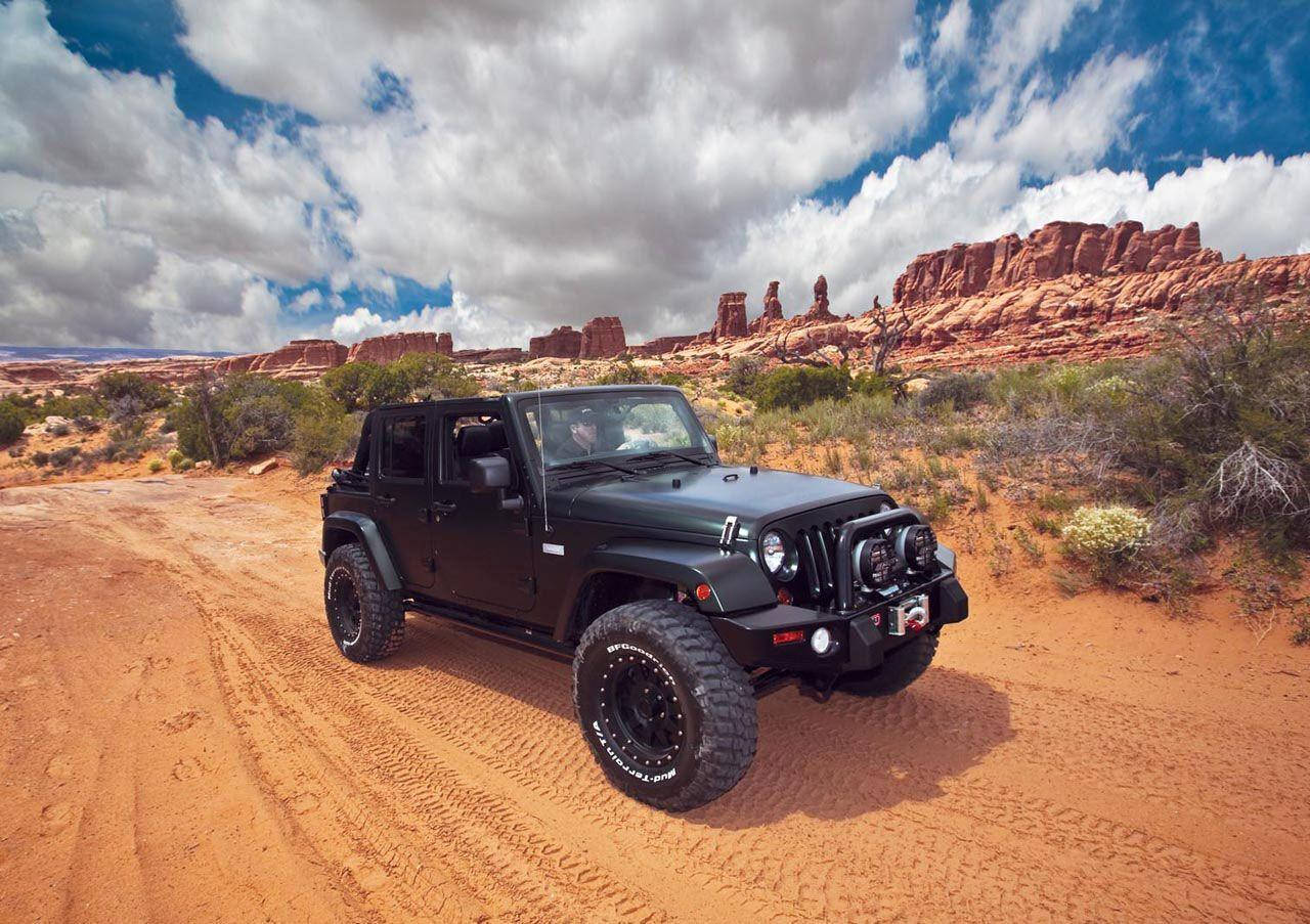Wrangler 桌布 壁紙 — 一輛黑色Jeep Wrangler在戲劇性的多雲天空下，穿越紅色沙漠地形，背景有岩石 formations。