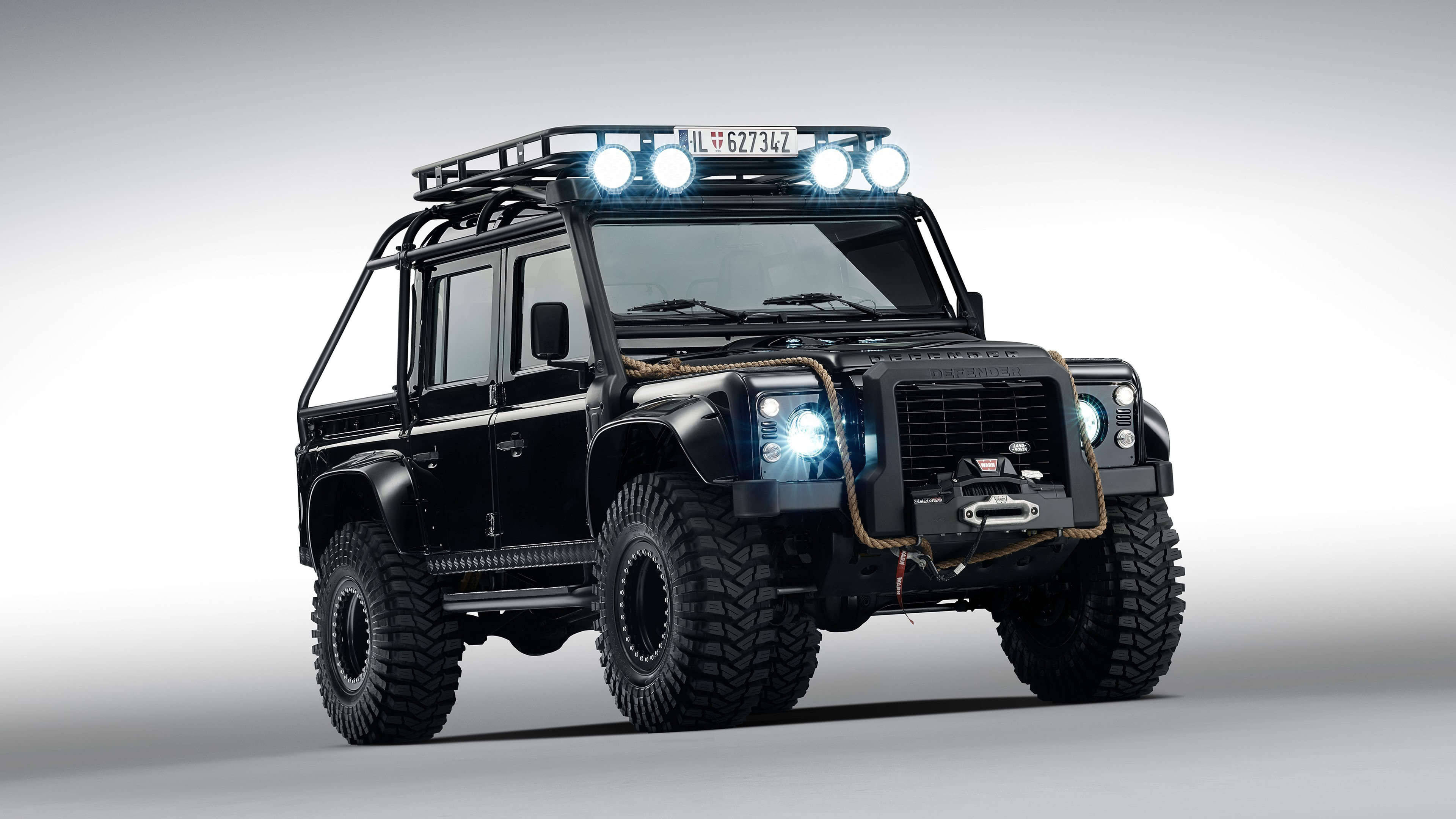 荒原路華 桌布 壁紙 — 一輛黑色Land Rover Defender配備車頂架和明亮車燈，在極簡灰色工作室背景前矗立。