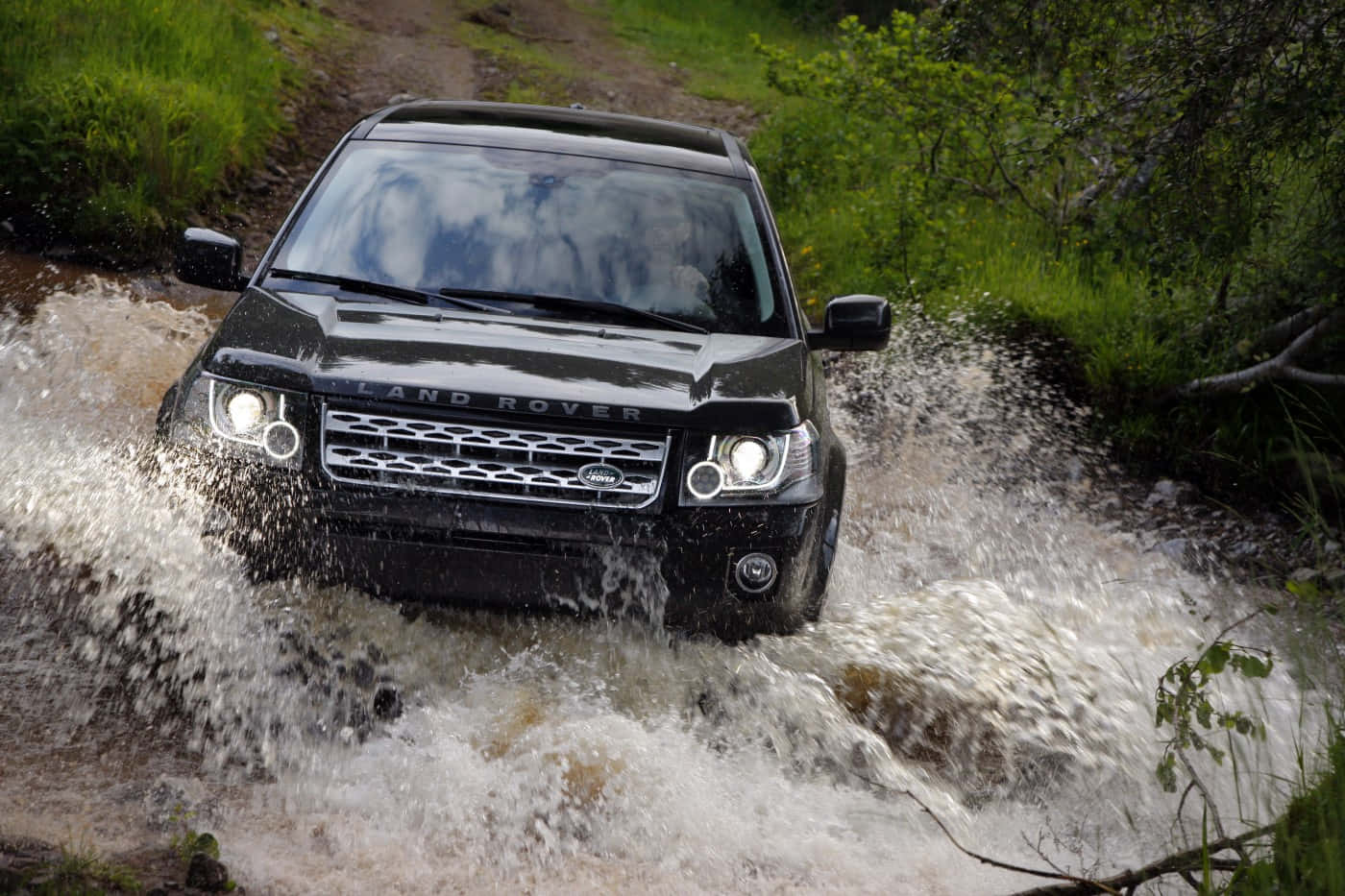 Land Rover Freelander 桌布 壁紙 — 一輛黑色Land Rover在泥濘的森林溪流中疾馳，水花四濺。