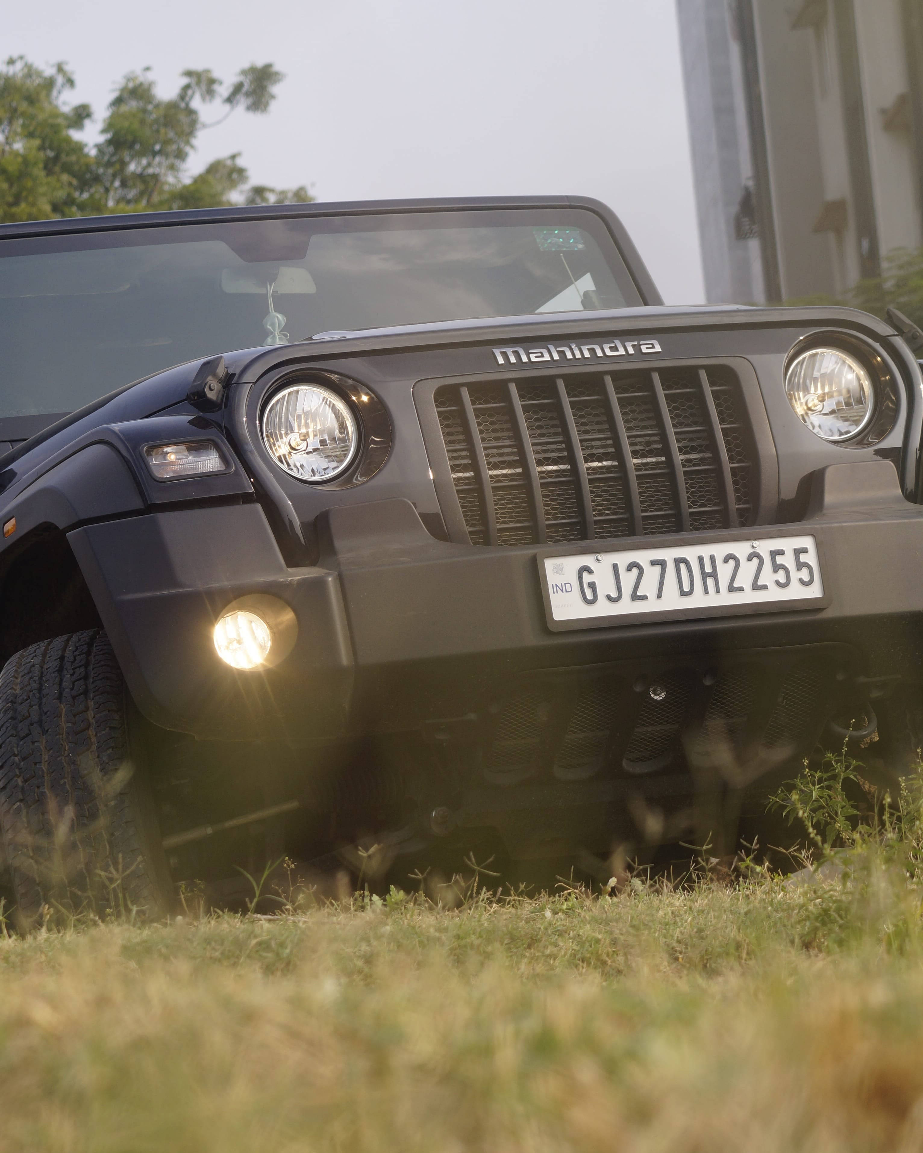 手機 桌布 壁紙 — 一輛黑色Mahindra Thar SUV停在草地上，車頭燈亮著，車牌GJ27DH2255清晰可見。