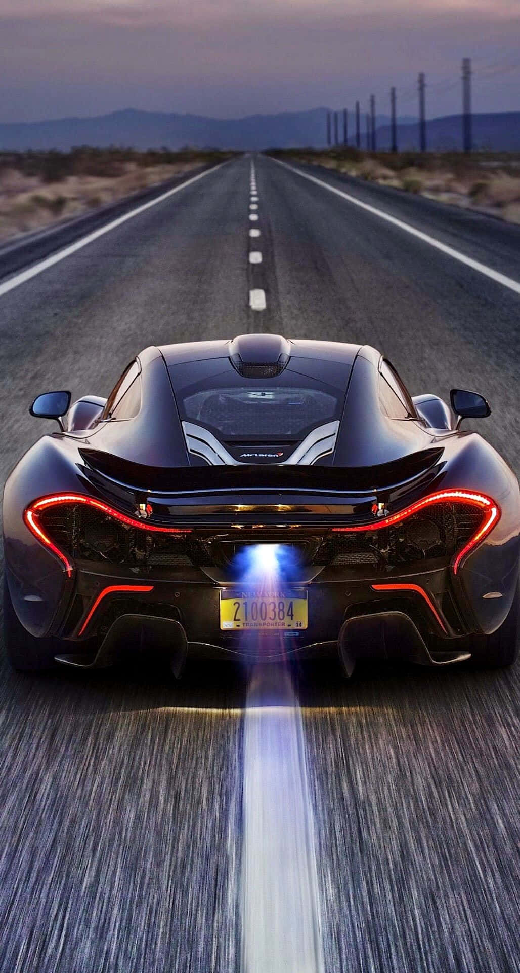 電玩遊戲 桌布 壁紙 — 一輛黑色McLaren P1在黃昏時分沿沙漠公路飛馳，帶有發光的紅色尾燈和藍色排氣火焰。
